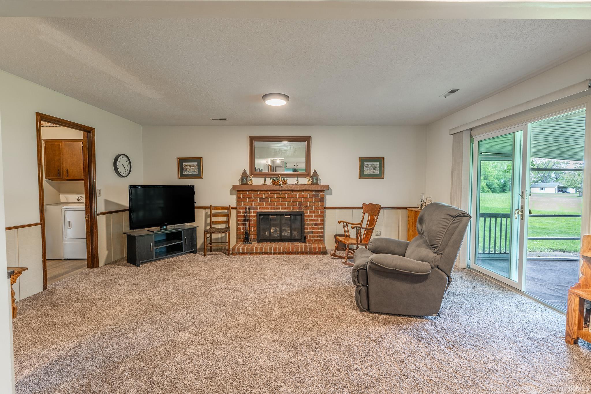 Carpeted living area featuring a brick fireplace with a wood mantle, white paneled wainscoting, and a sliding glass door leading to an outdoor space