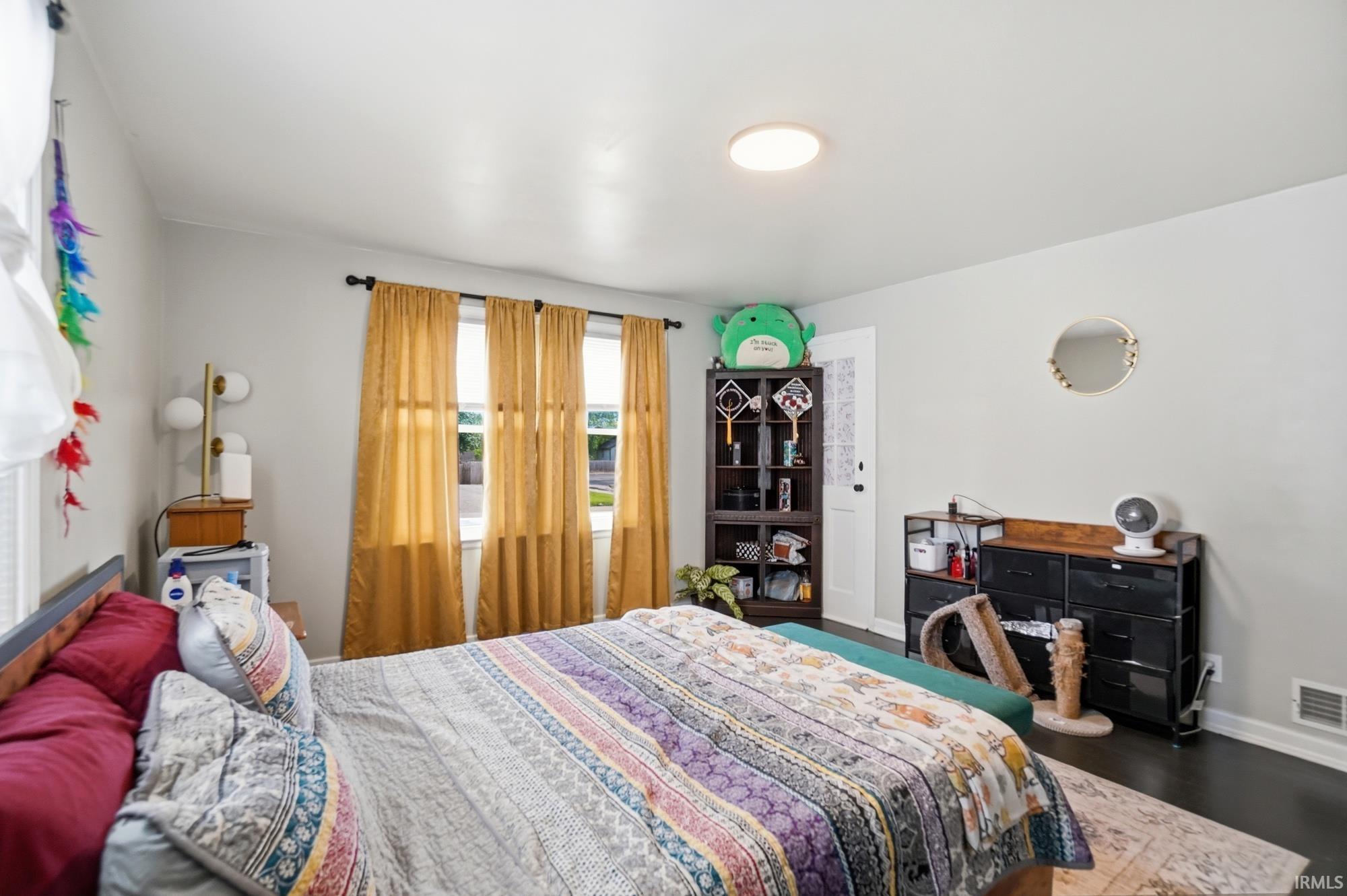 Bedroom featuring dark wood-finish flooring, light neutral-toned walls, a ceiling-mounted flush light fixture, and multiple windows