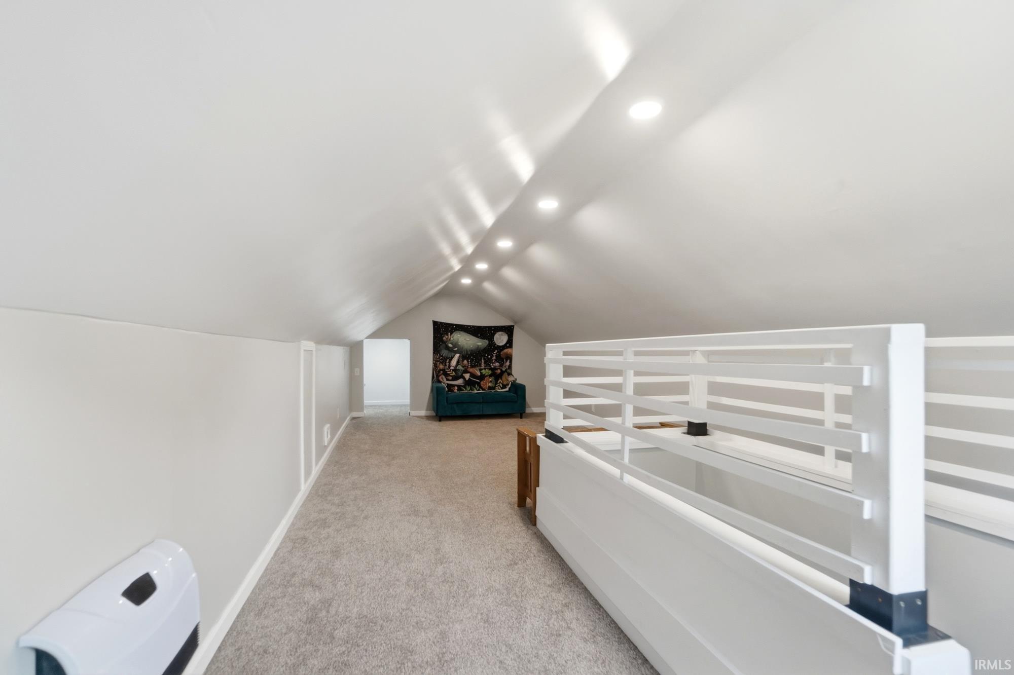 Spacious bonus room featuring sloped ceilings, recessed lighting, neutral carpet flooring, and a white slatted railing