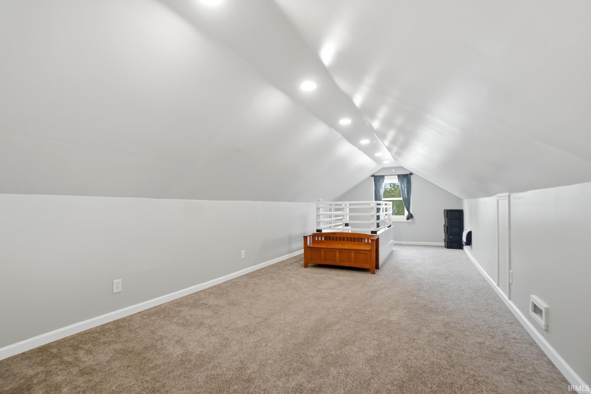 Spacious carpeted room featuring vaulted ceilings, recessed lighting, a single window, and light grey walls