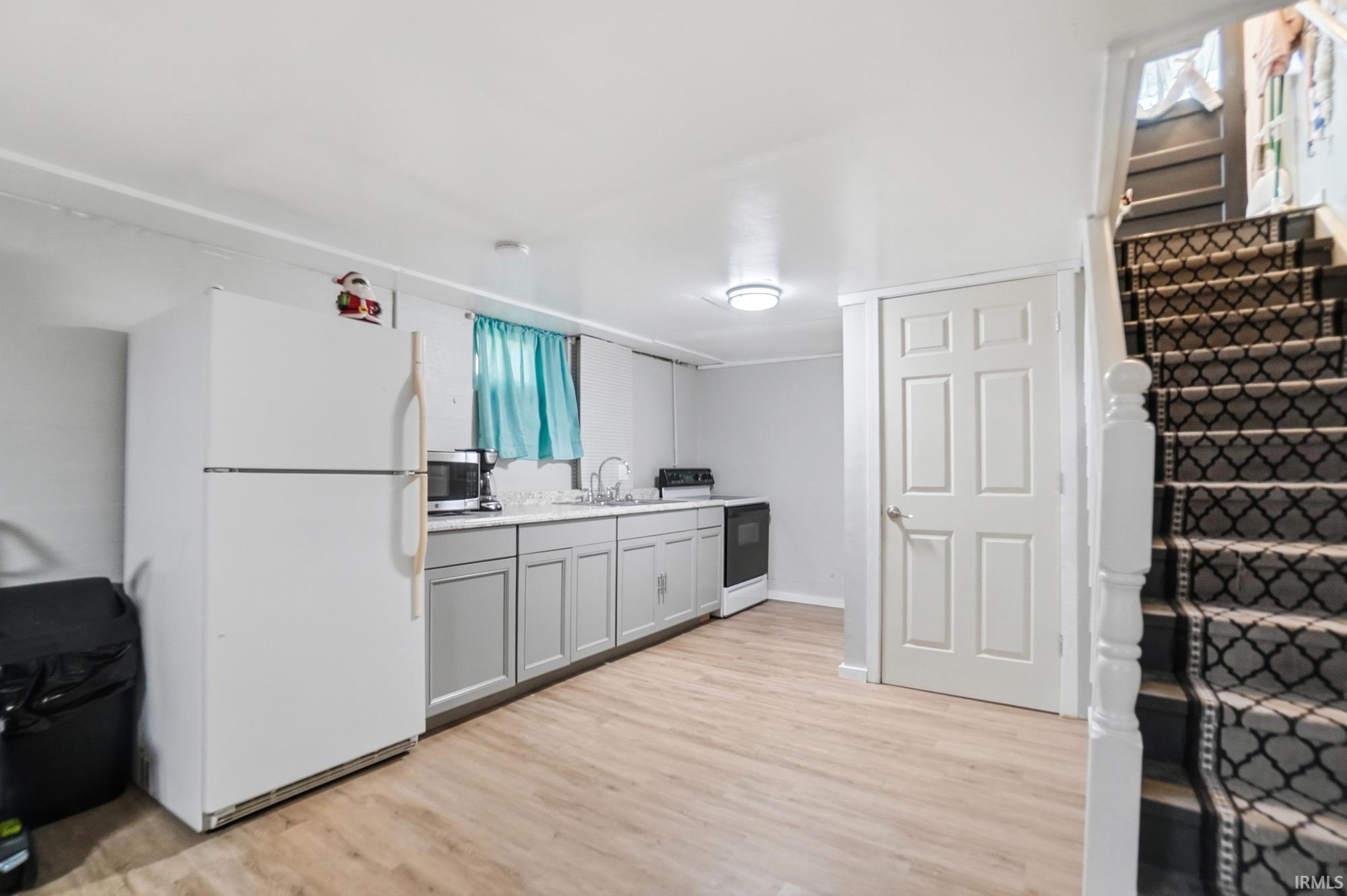 Kitchenette featuring light wood-finish flooring, white refrigerator, gray base cabinets, and a white sink