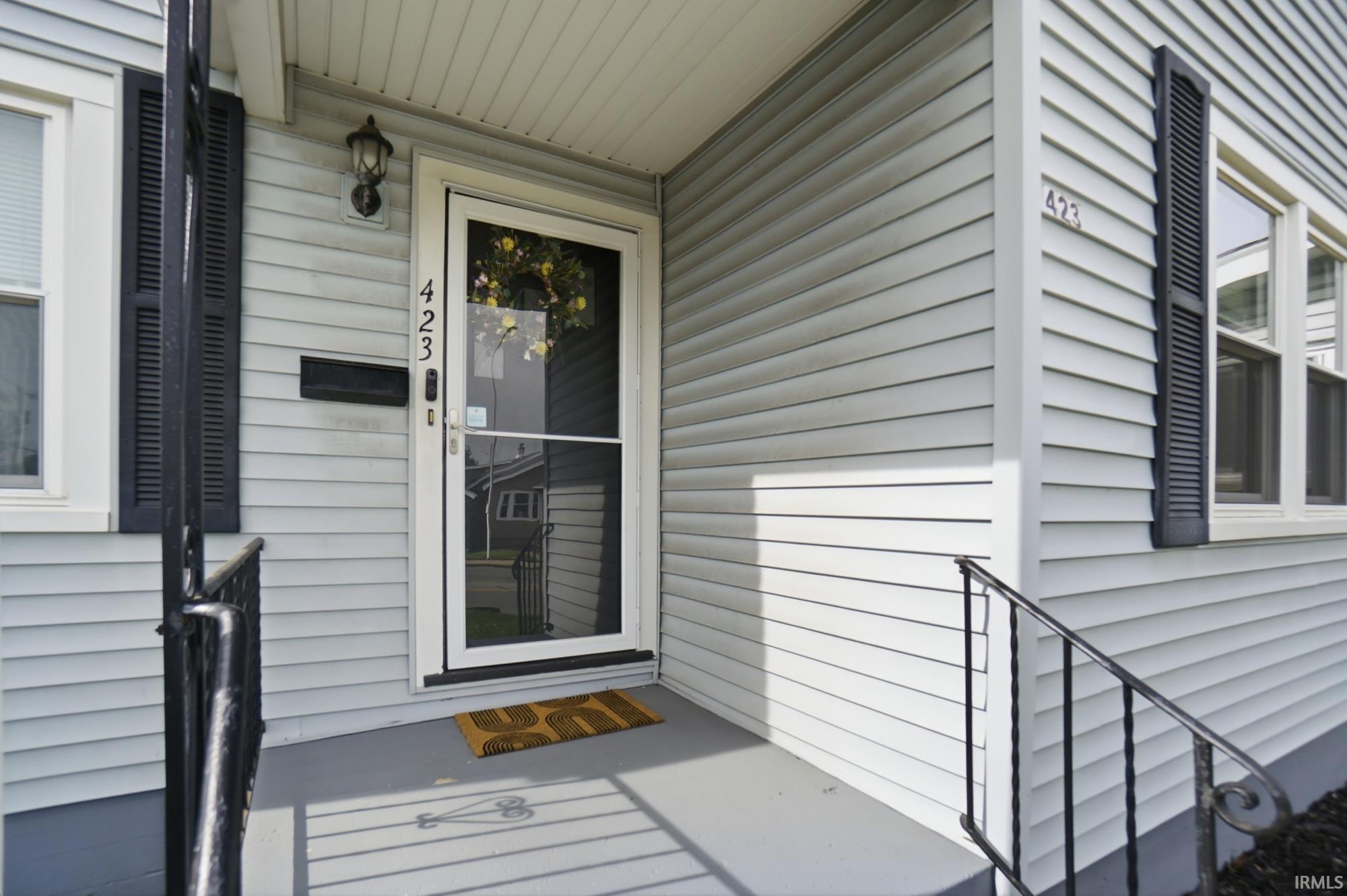 Front entry with a storm door, an exterior wall light, and a mailbox