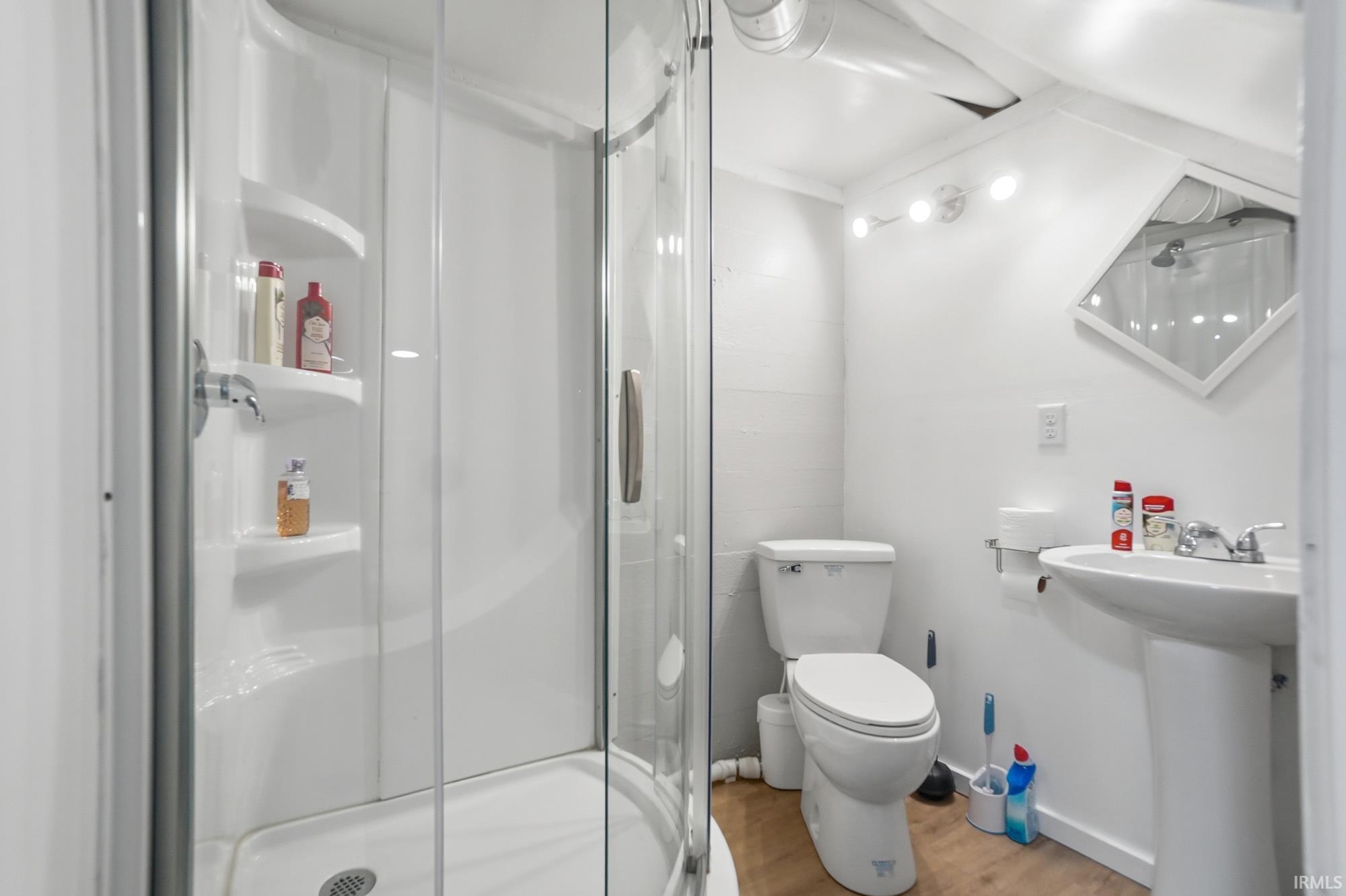 Bathroom featuring a glass-enclosed shower with integrated shelving, pedestal sink, and wood-finish flooring