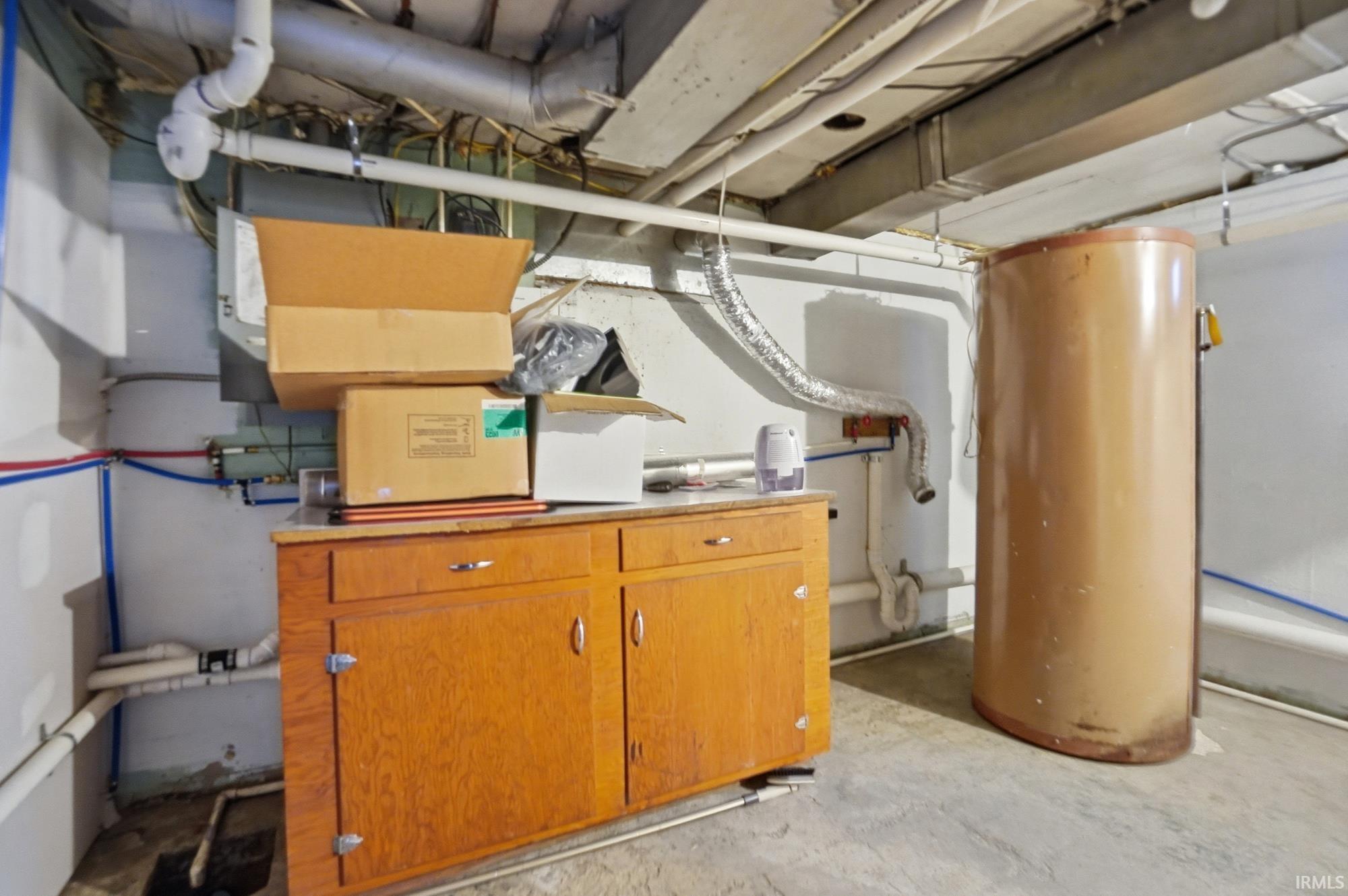 Basement utility area featuring a hot water heater, exposed overhead ductwork, and a built-in wood-finish cabinet with white countertops