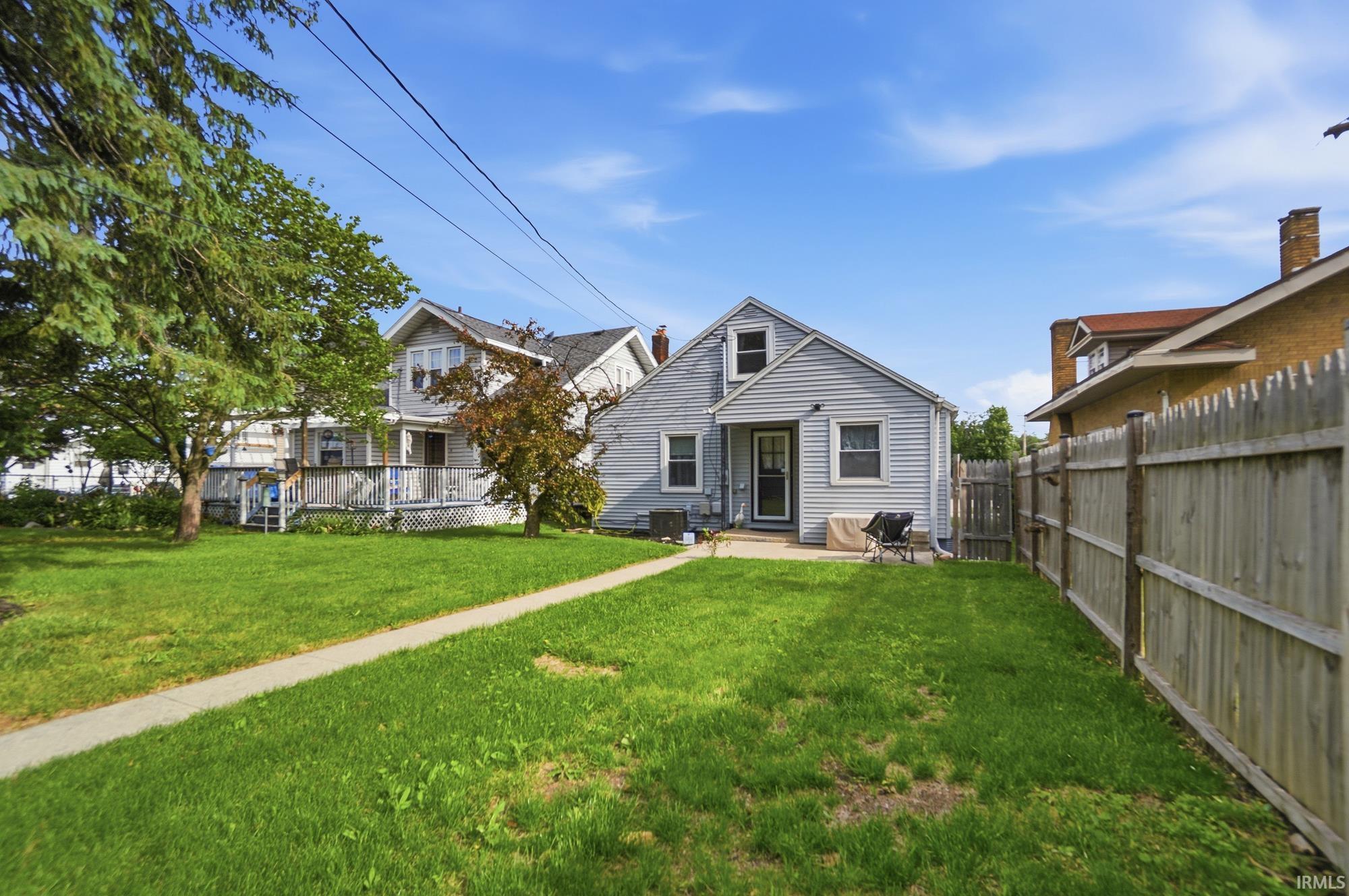 Expansive green lawn with a concrete pathway leading to the rear entrance of a light-colored siding home