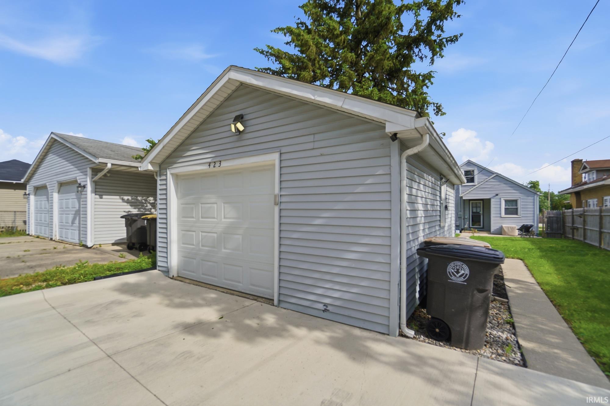 Detached single-car garage featuring light gray siding and a paneled white overhead door with exterior lighting