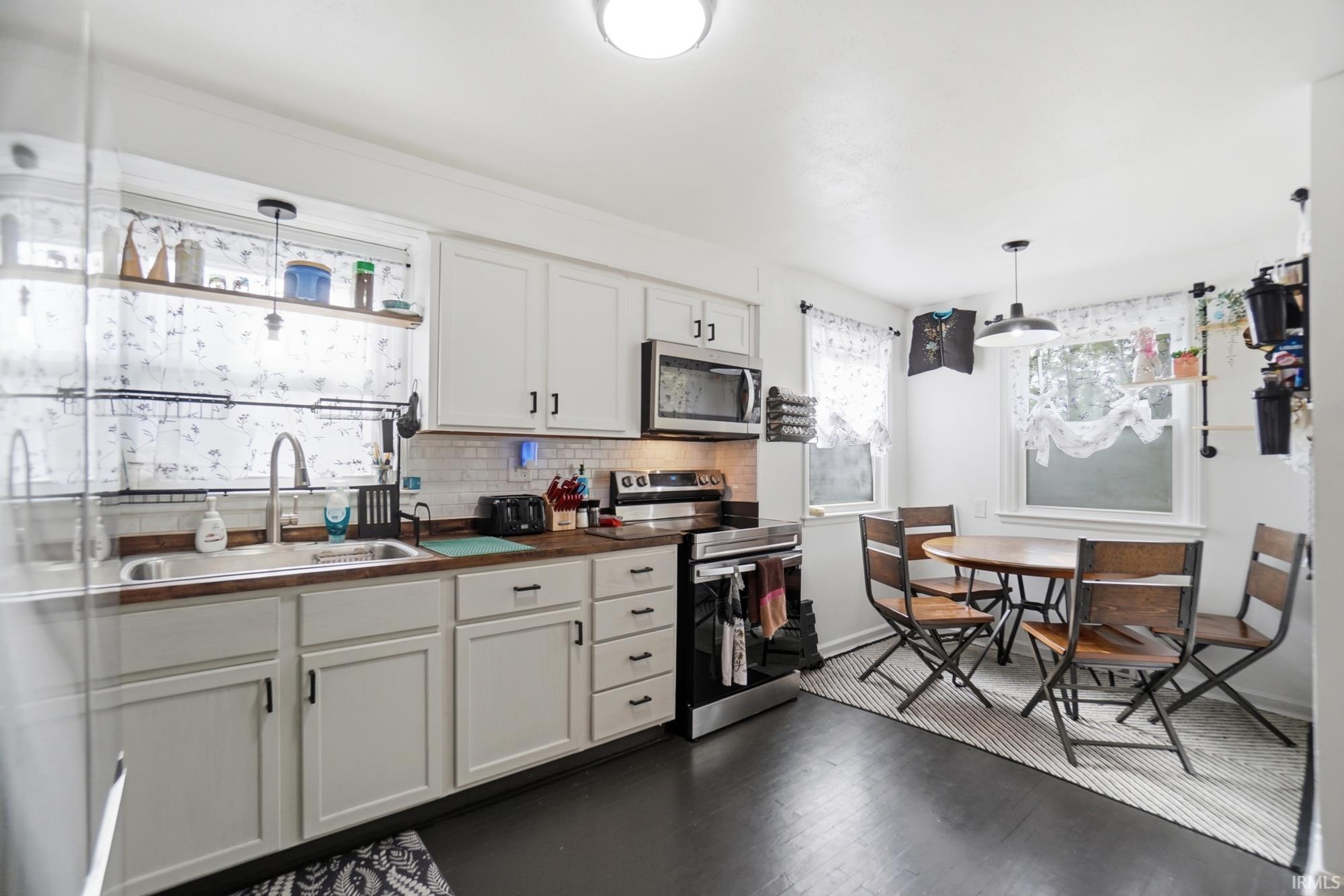Kitchen featuring white cabinetry, subway tile backsplash, wood-finish countertops, stainless steel appliances, and dark wood-finish flooring