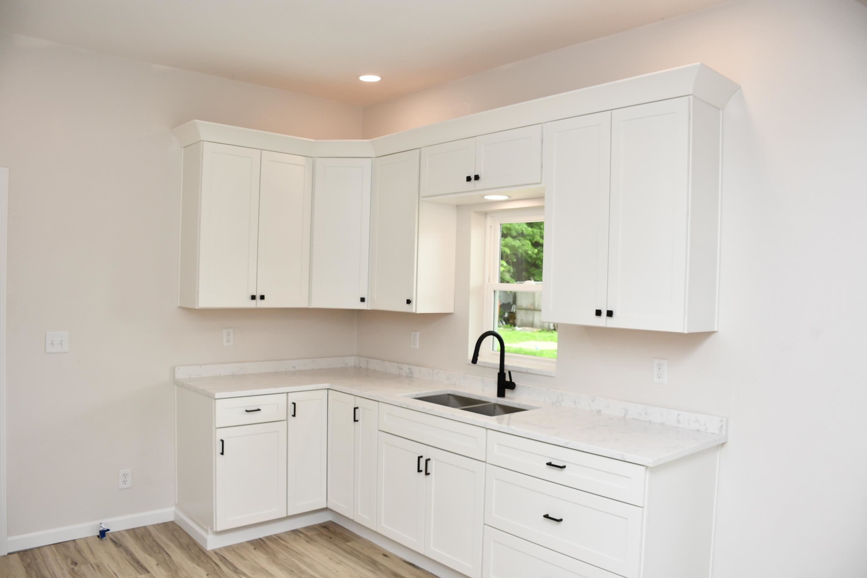 Contemporary kitchen featuring white cabinetry with black hardware, a double basin sink, and solid surface countertops