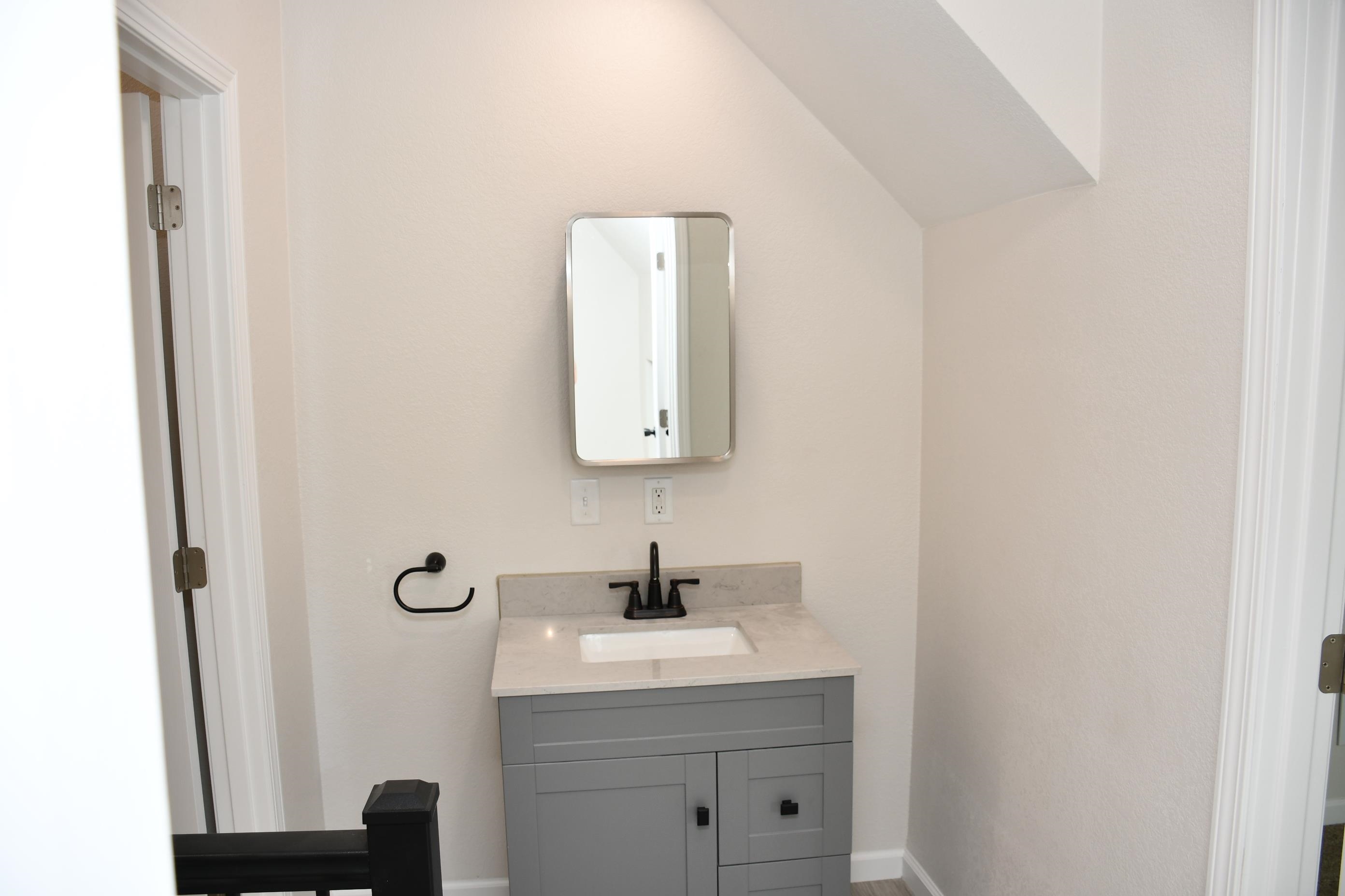 Modern vanity featuring a gray cabinet with black hardware, a rectangular sink, and a light-toned countertop