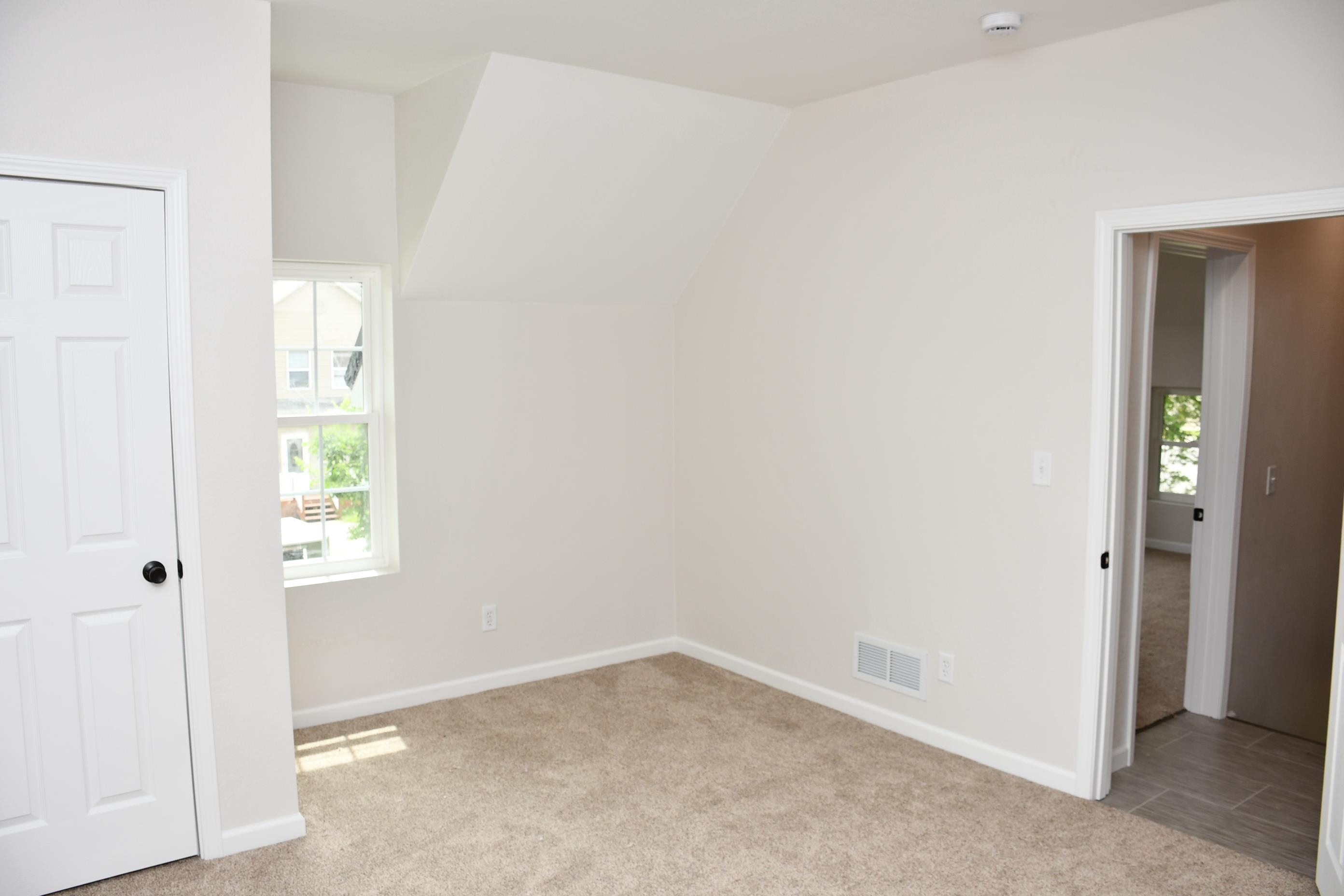 Carpeted room featuring a double-pane window, white trim, and a white six-panel door with black hardware