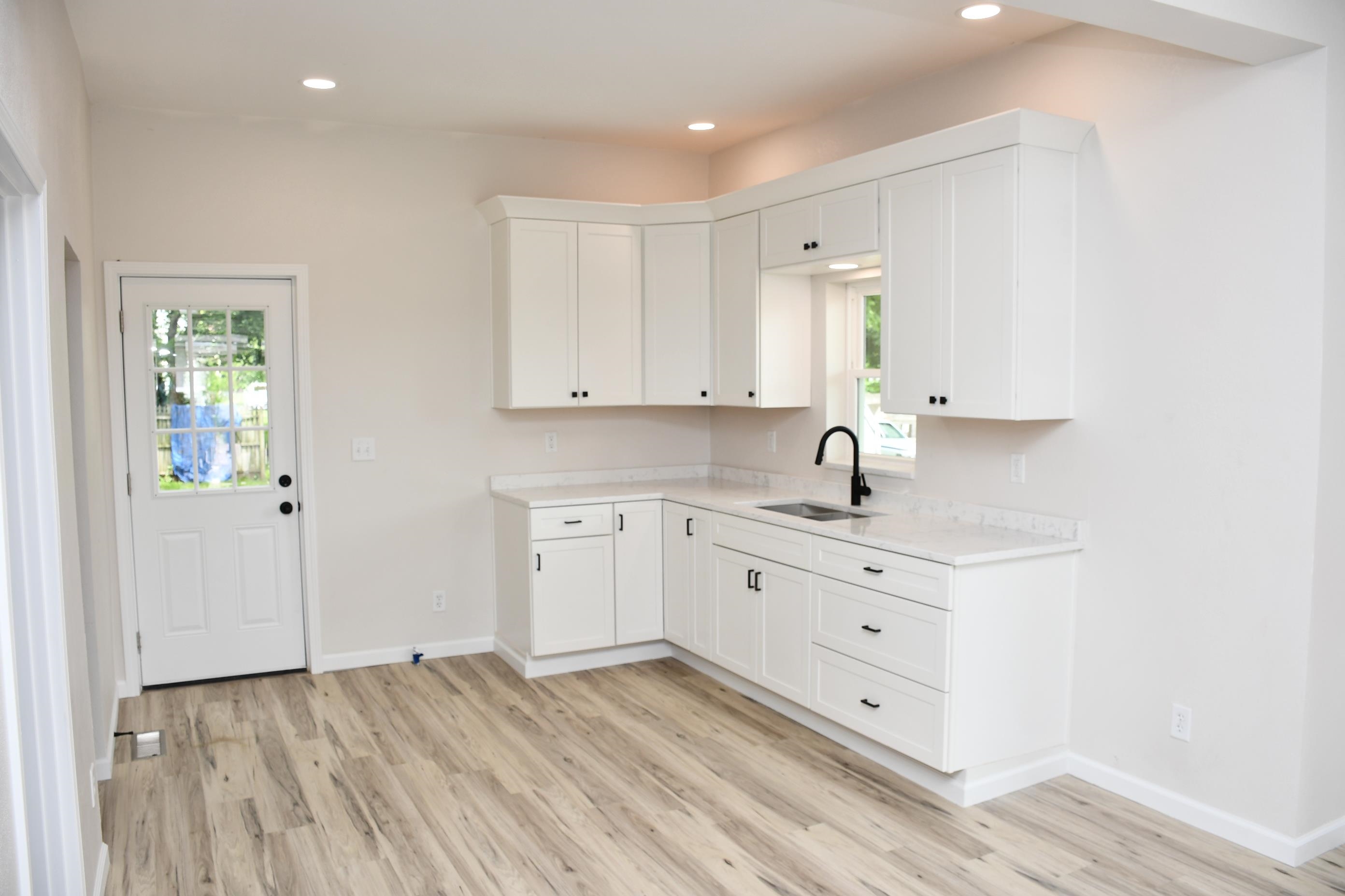 Modern kitchen featuring white shaker-style cabinetry, light-toned wood-finish flooring, recessed lighting, and a black gooseneck faucet