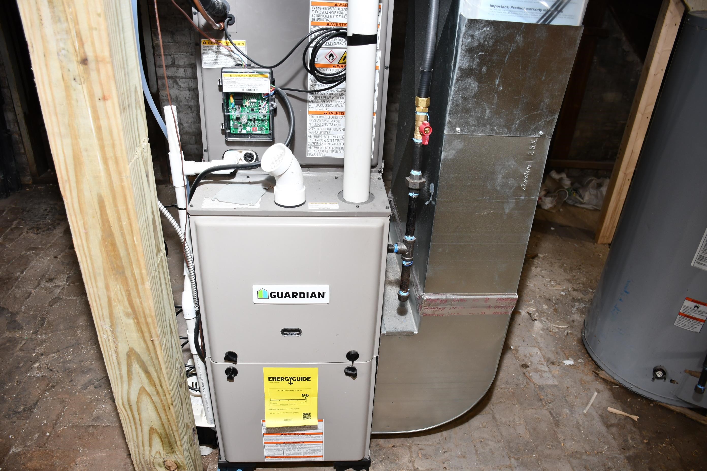 Guardian brand furnace with an EnergyGuide label, associated ductwork, and plumbing components