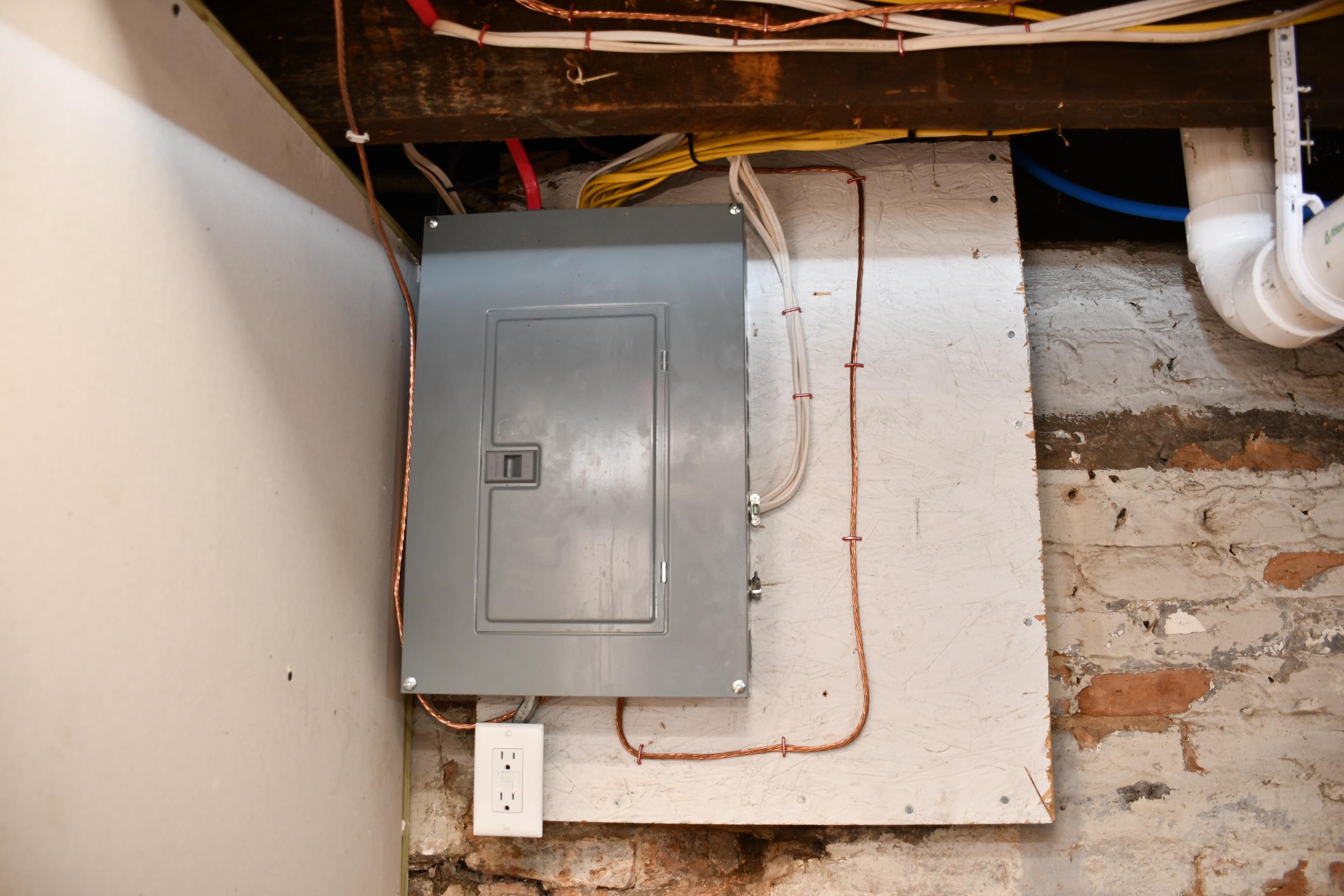 Electrical panel and exposed wiring, with a wall outlet mounted below
