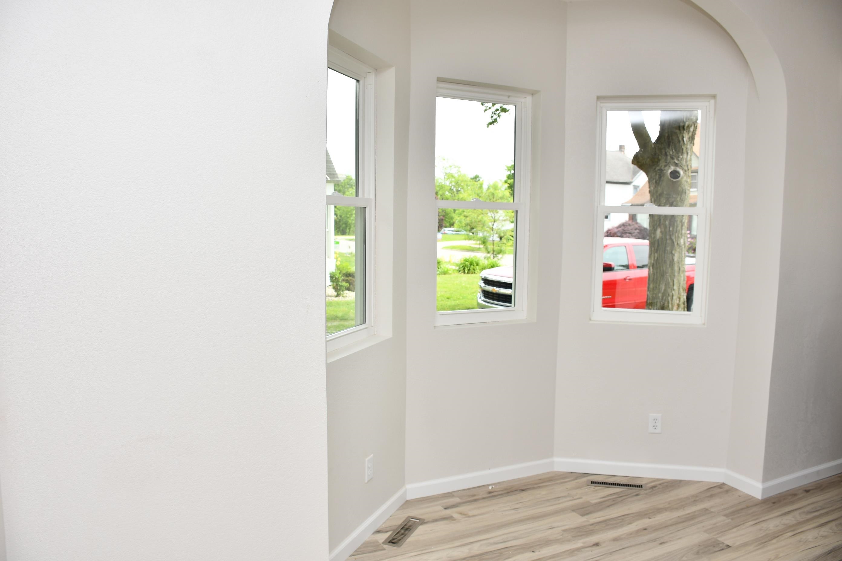 Corner space featuring three double-hung windows, light wood-finish flooring, white baseboards, and white painted walls