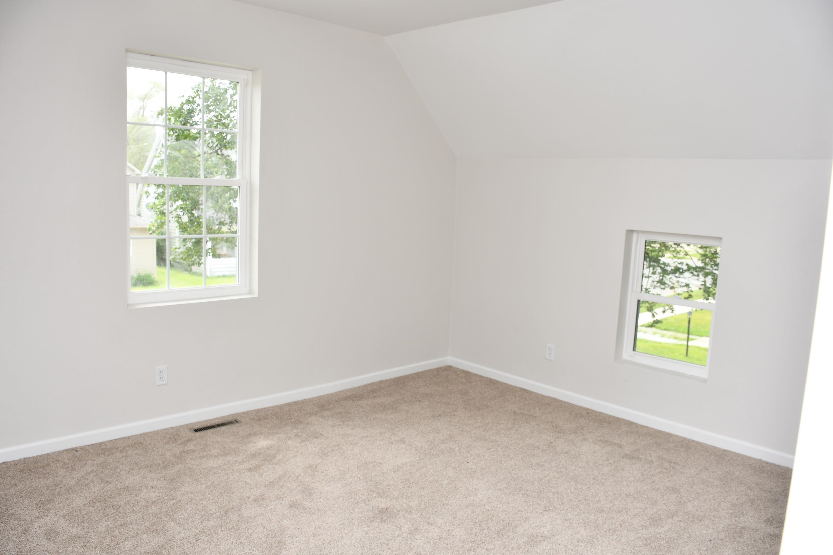 Carpeted room featuring two windows, vaulted ceiling, and white baseboards