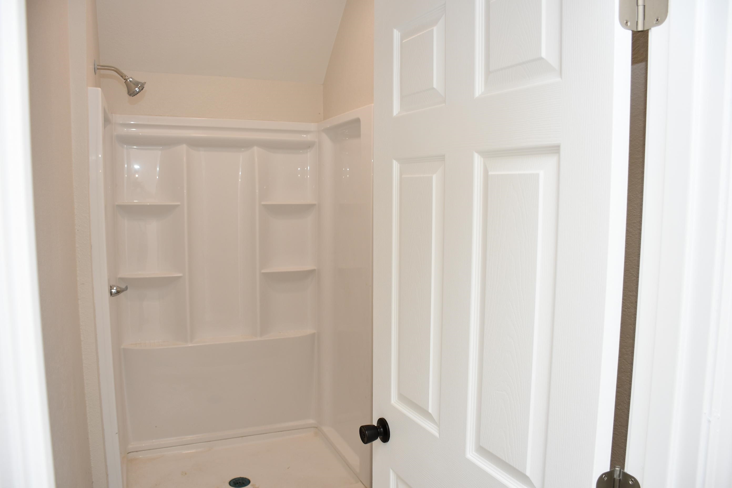 White fiberglass shower stall with integrated shelving, chrome showerhead, and matching handle