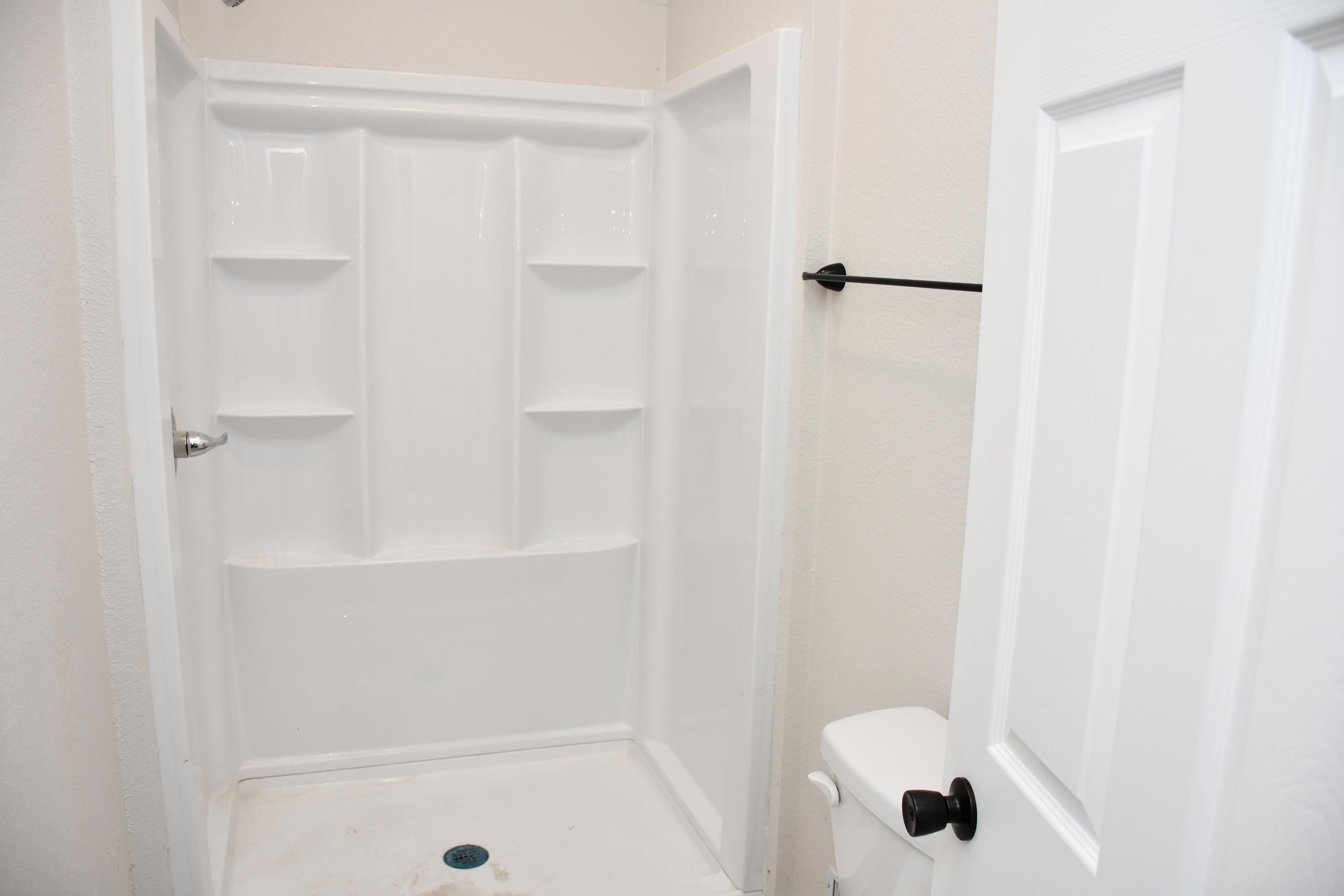 White one-piece shower unit with integrated shelving, matte black towel bar, and a white paneled door with matte black hardware