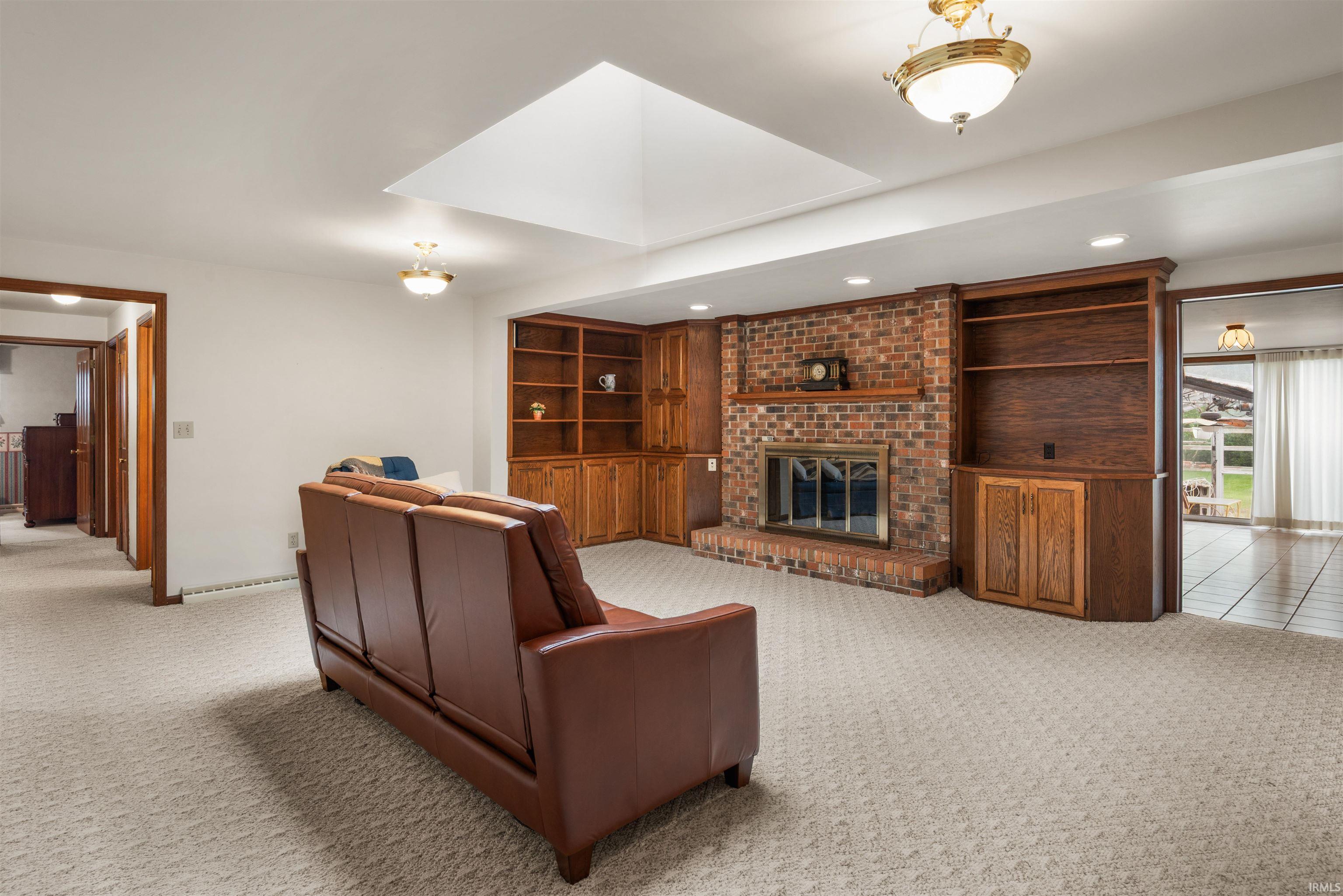 Carpeted living area featuring a brick fireplace with a mantel, built-in wood cabinetry, a recessed ceiling with a skylight, and overhead lighting