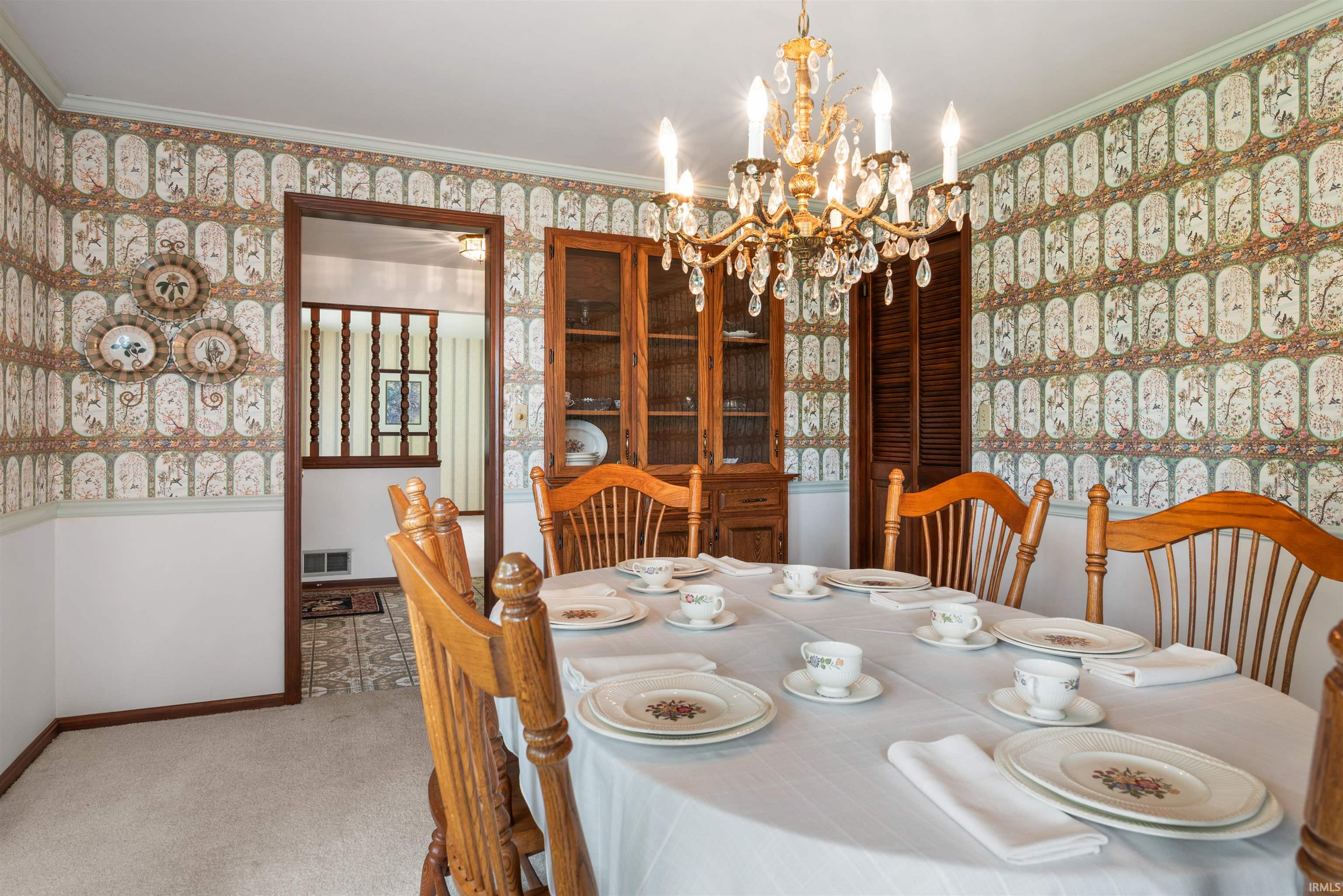 Dining area featuring a crystal chandelier, patterned wallpaper with a chair rail, light-colored carpet, and a built-in wooden hutch