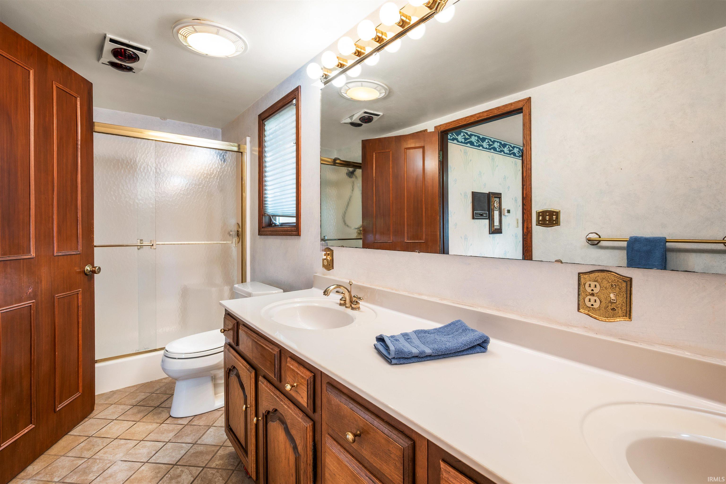 Dual vanity with integrated sinks, wood-finish cabinetry, and a large wall-mounted mirror