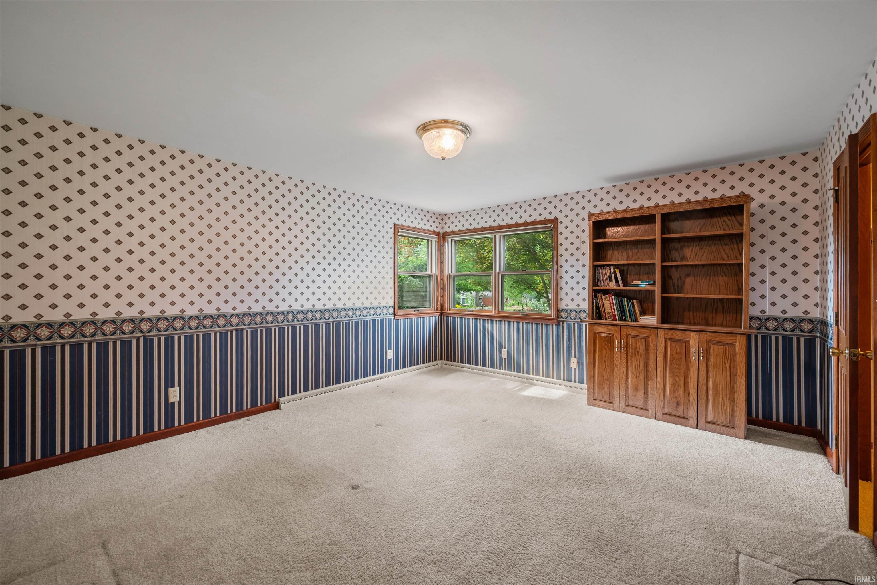 Spacious room featuring a multi-paned window, built-in wooden cabinetry with shelving, wall sconce lighting, and carpeted flooring