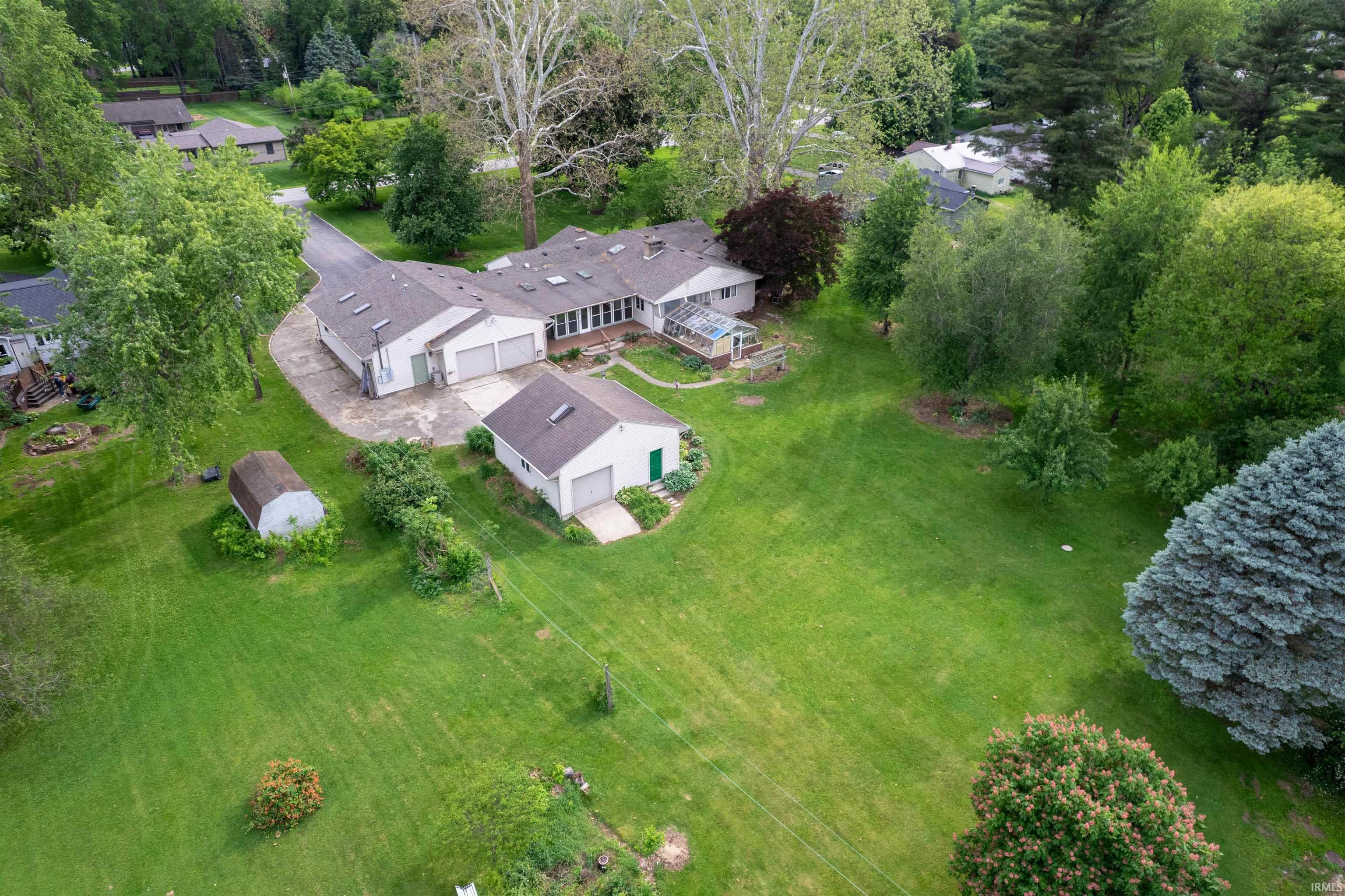 Sprawling property featuring a primary residence with multiple skylights, an attached garage, a detached garage, a separate storage shed, and extensive green space with mature trees
