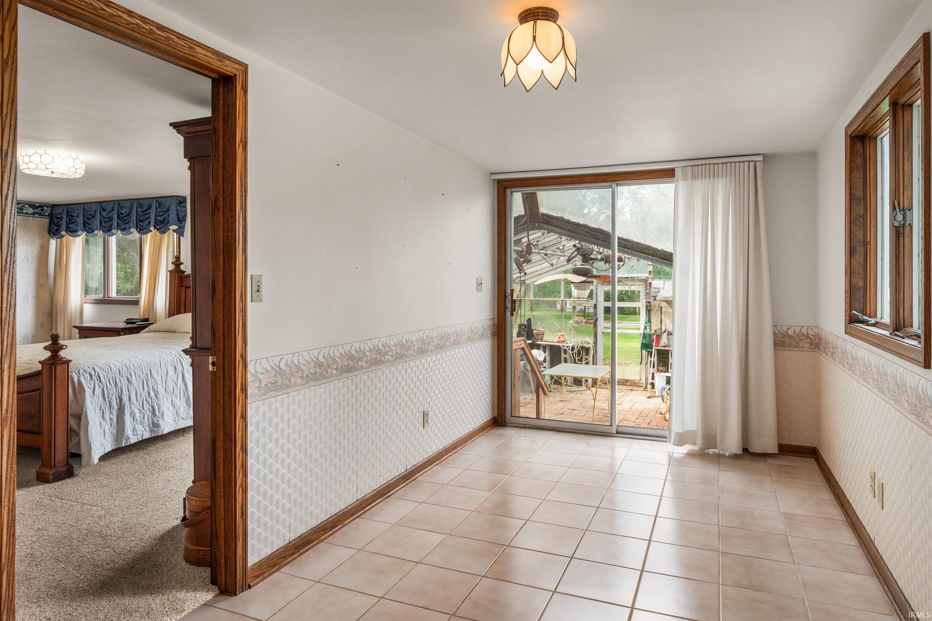 Tiled flooring room featuring sliding glass doors to the exterior, a single window with wood framing, and an overhead light fixture