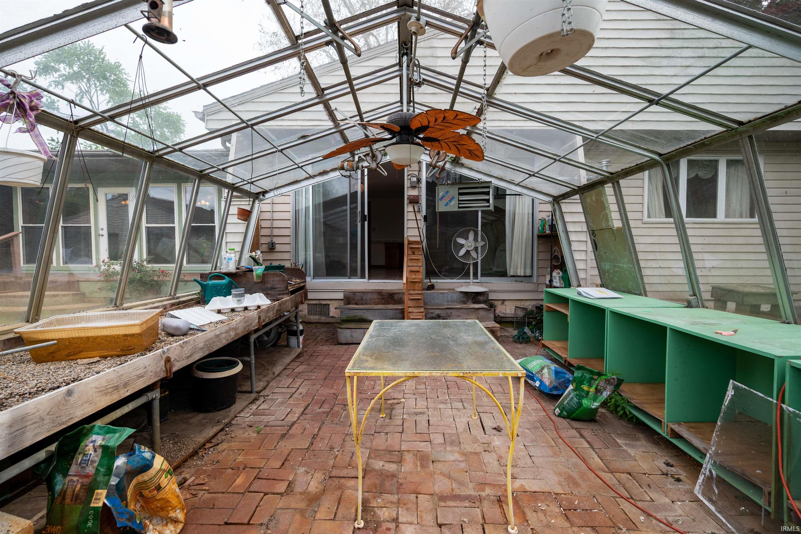 Glass-paneled solarium with brick flooring, multiple built-in shelving units, and an overhead ceiling fan