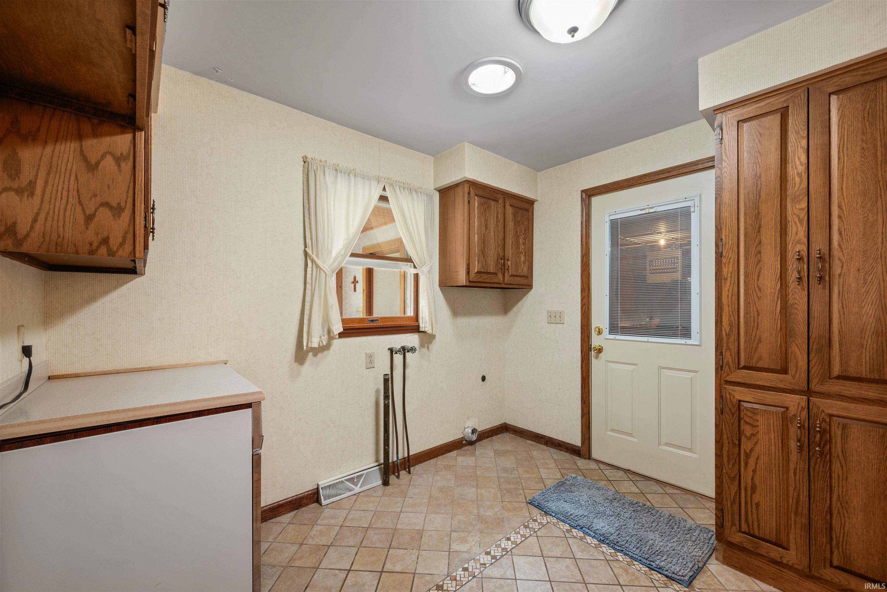Functional utility room featuring tile flooring, a window with natural wood trim, and extensive wood cabinetry