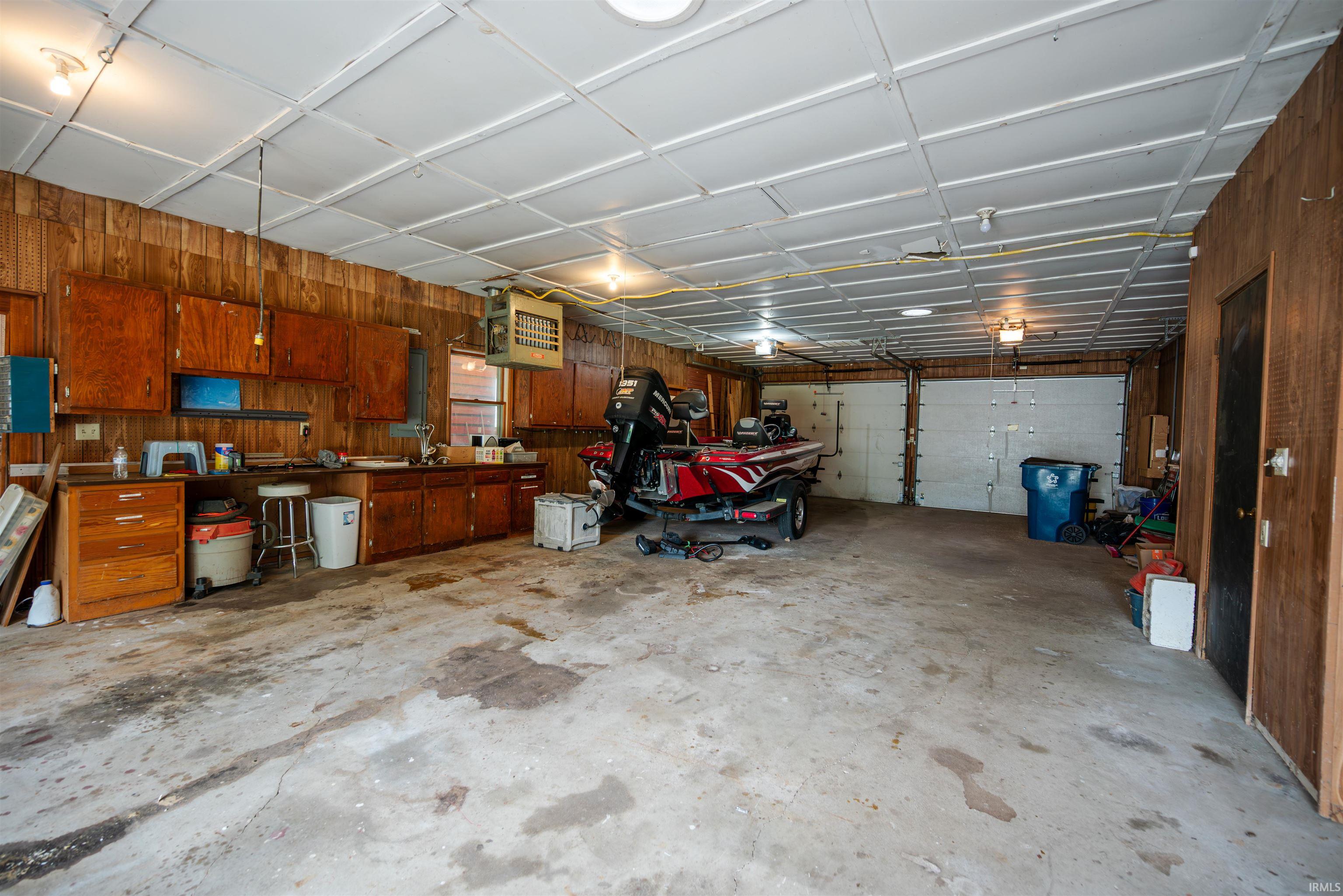 Spacious garage featuring two overhead doors, concrete flooring, wood-paneled walls, and built-in cabinetry with ample storage