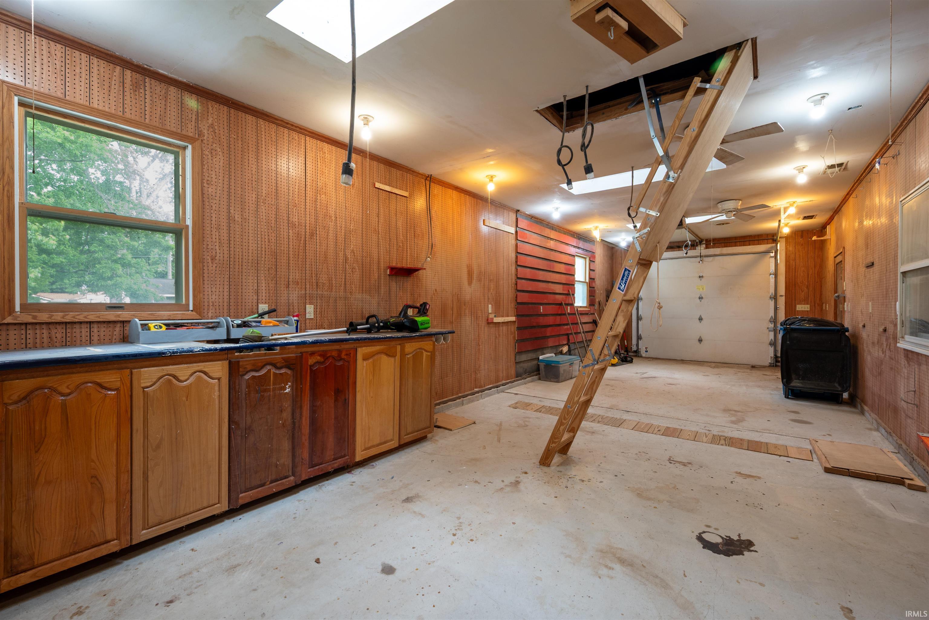 Garage interior featuring wood paneling, a built-in workbench with cabinetry, concrete flooring, a skylight, and an overhead garage door