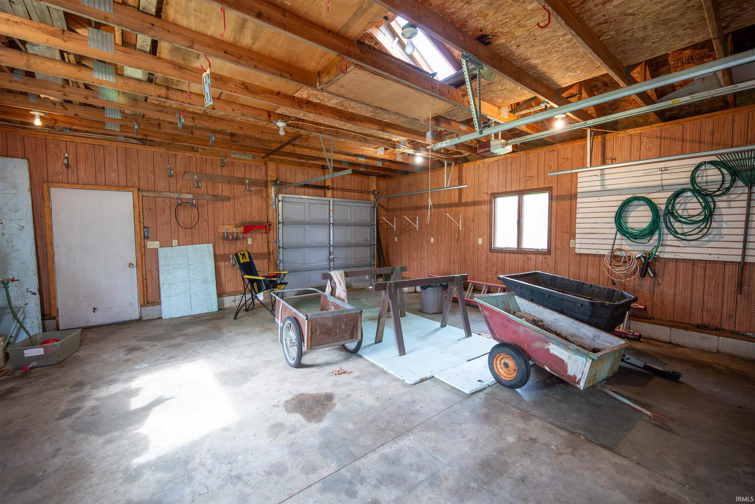 Spacious garage featuring a concrete floor, wood-paneled walls, exposed ceiling beams, and a skylight