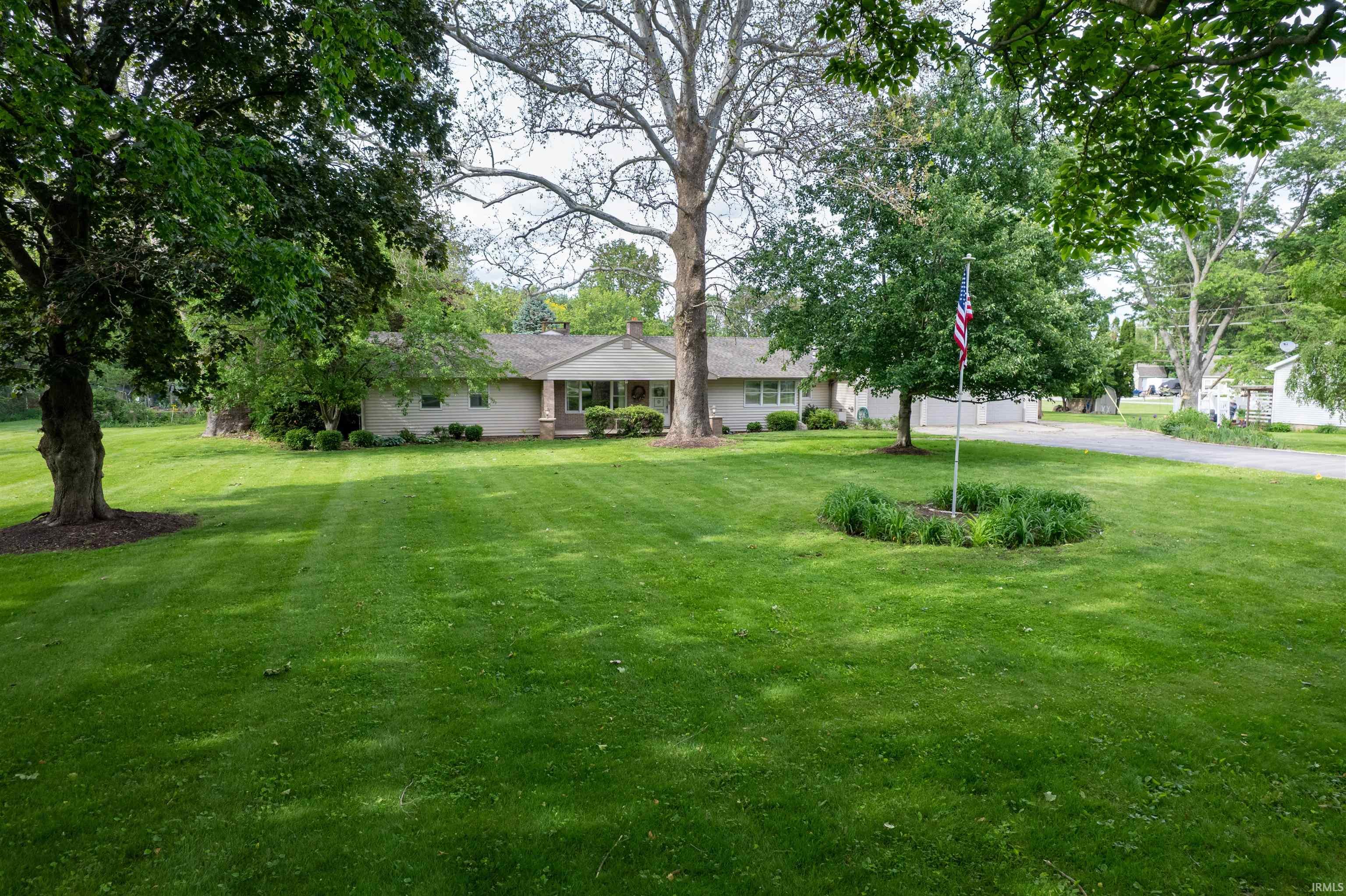 Expansive front lawn featuring mature trees and a flag pole