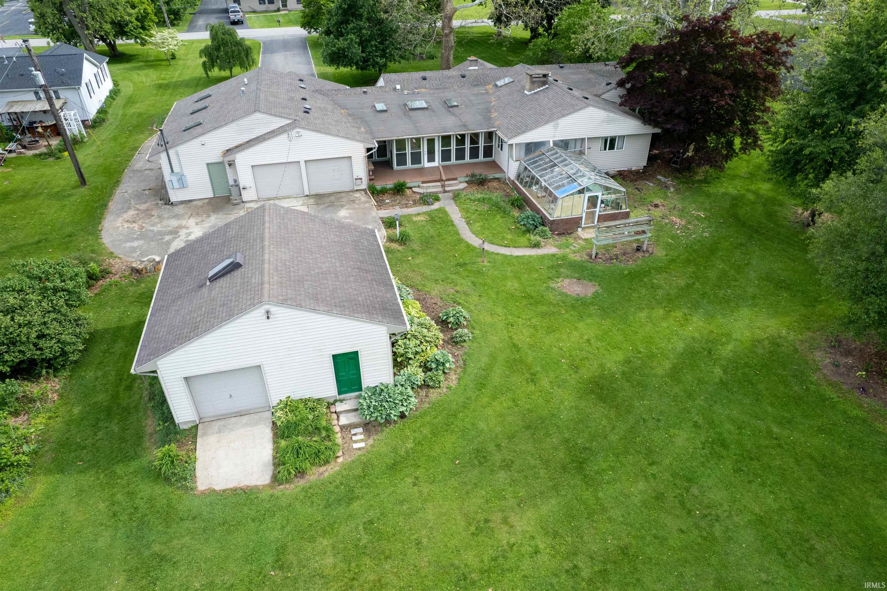 Expansive property featuring a multi-car garage, separate outbuilding with garage door, dedicated greenhouse structure, and a large grass lawn