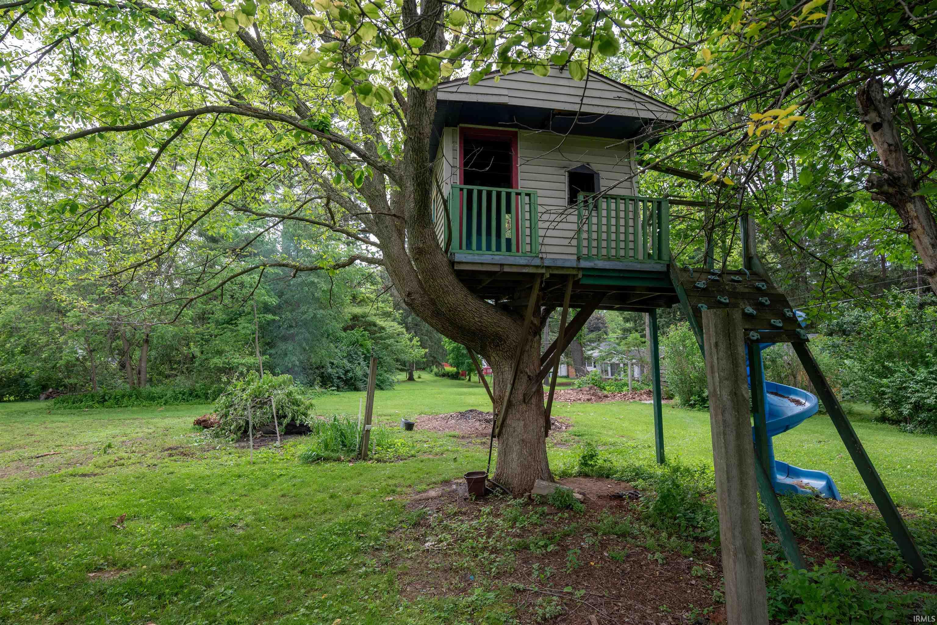 Expansive backyard featuring a treehouse with a balcony, spiral slide, and wooden ladder access