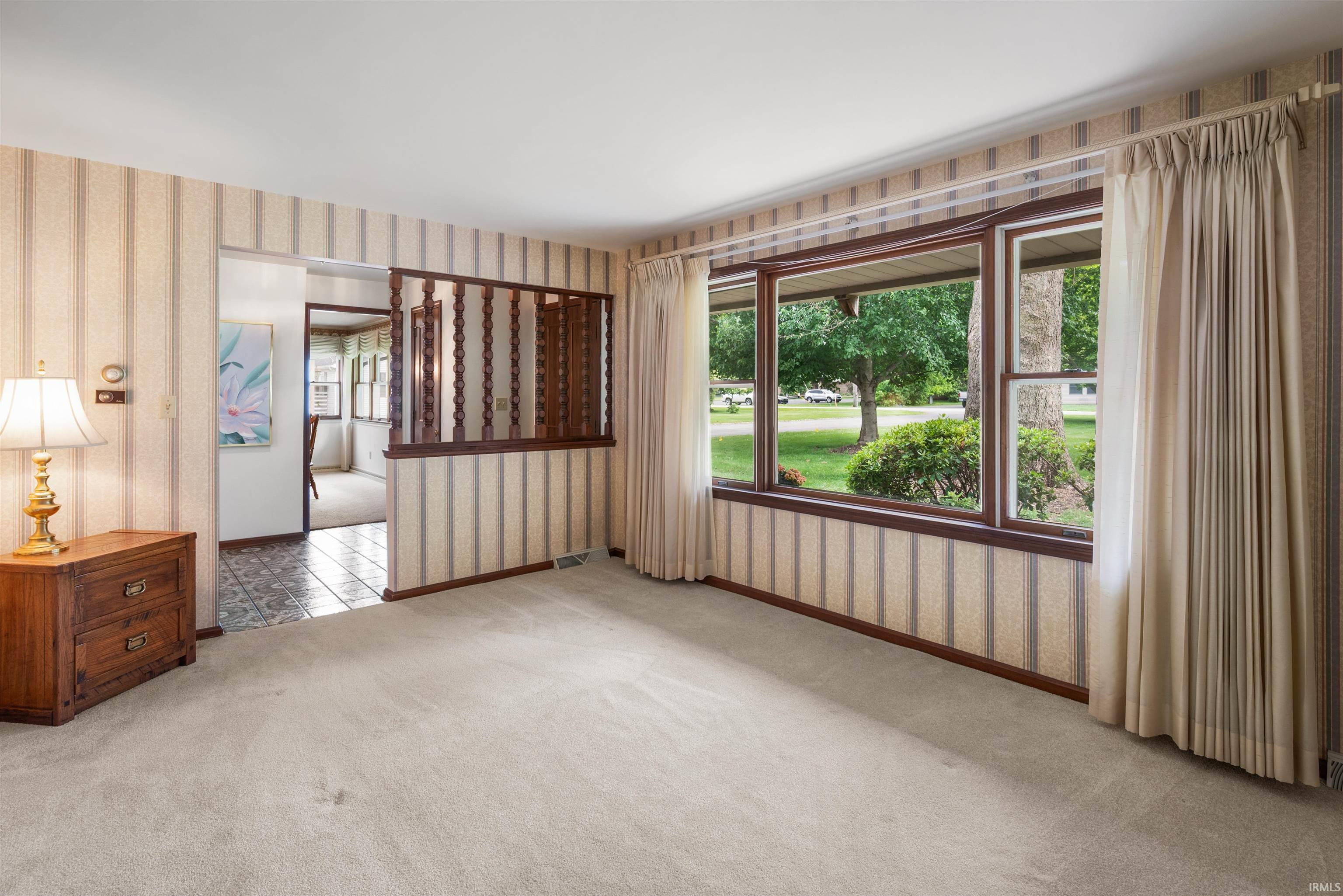 Carpeted living space featuring a picture window, patterned wallpaper, and wood-toned trim