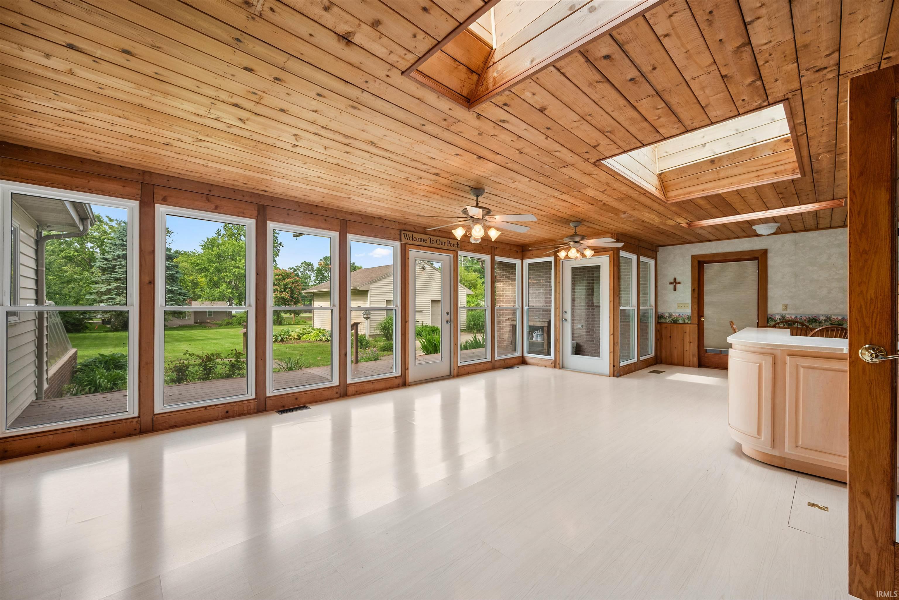 Sunroom featuring wood-paneled ceiling, skylights, white flooring, and multiple windows overlooking exterior grounds