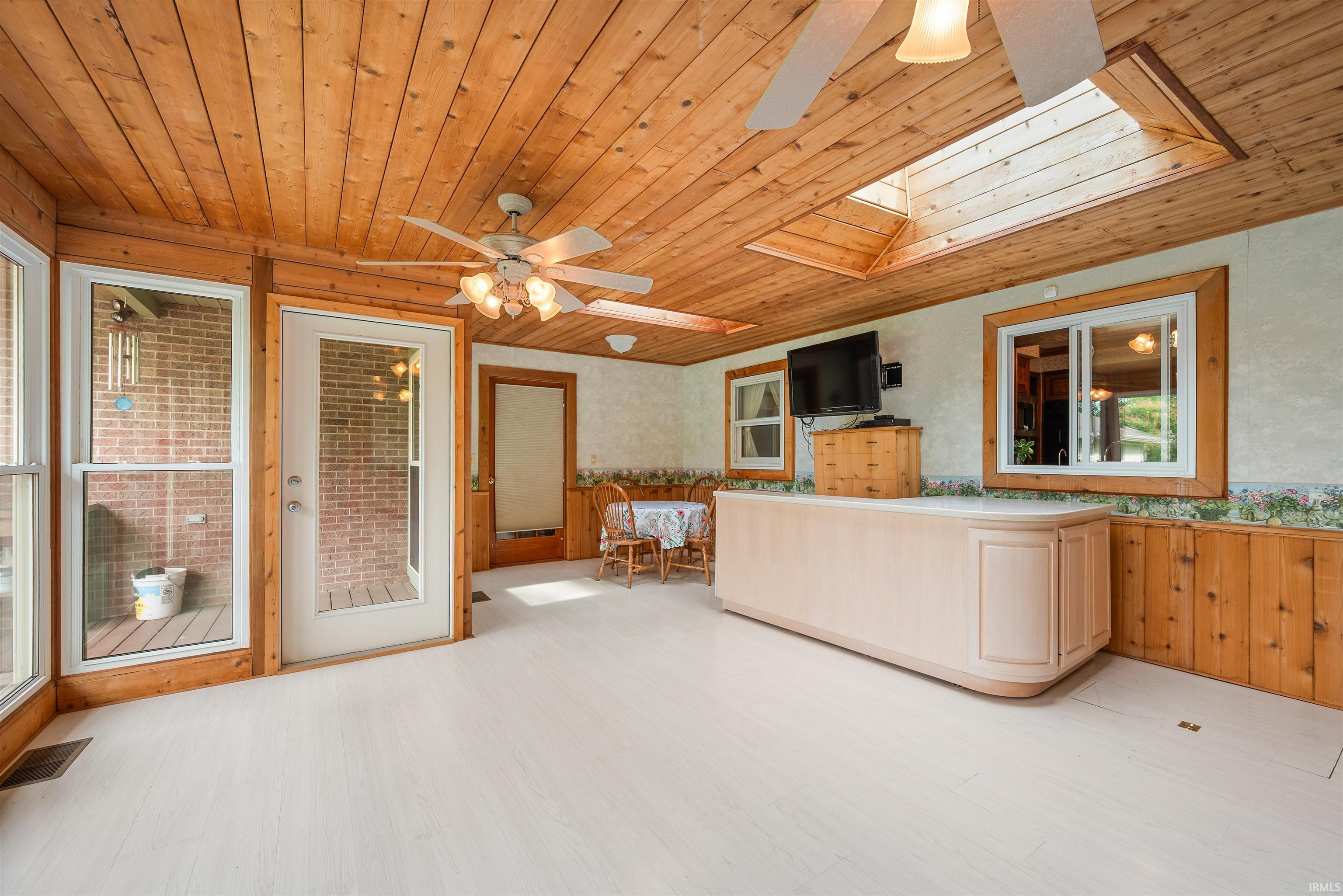 Sunroom featuring white wood-finish flooring, wood plank ceiling, and a skylight
