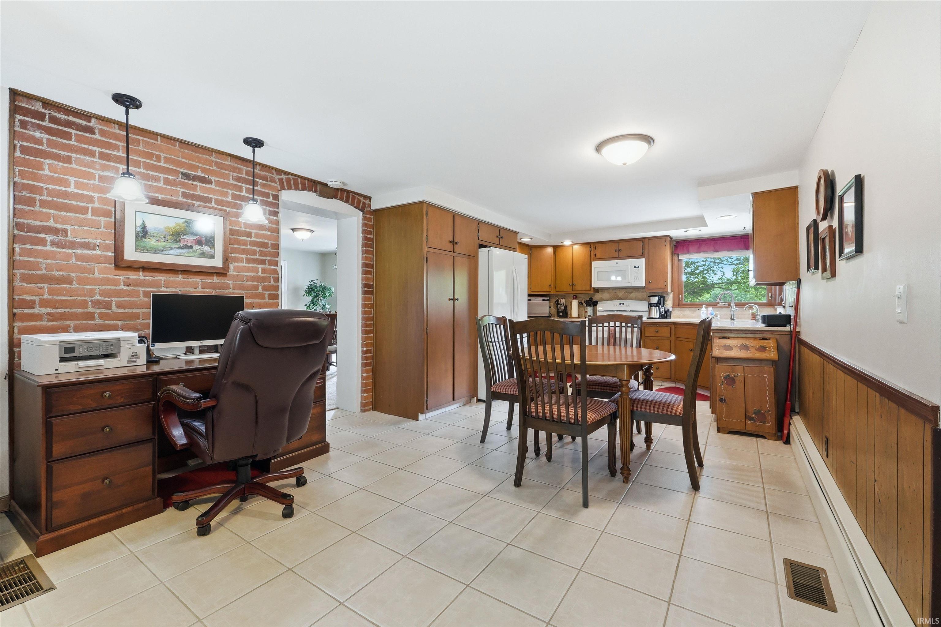 Open-concept area featuring brick accent wall, tiled flooring, wood cabinetry, and a white refrigerator