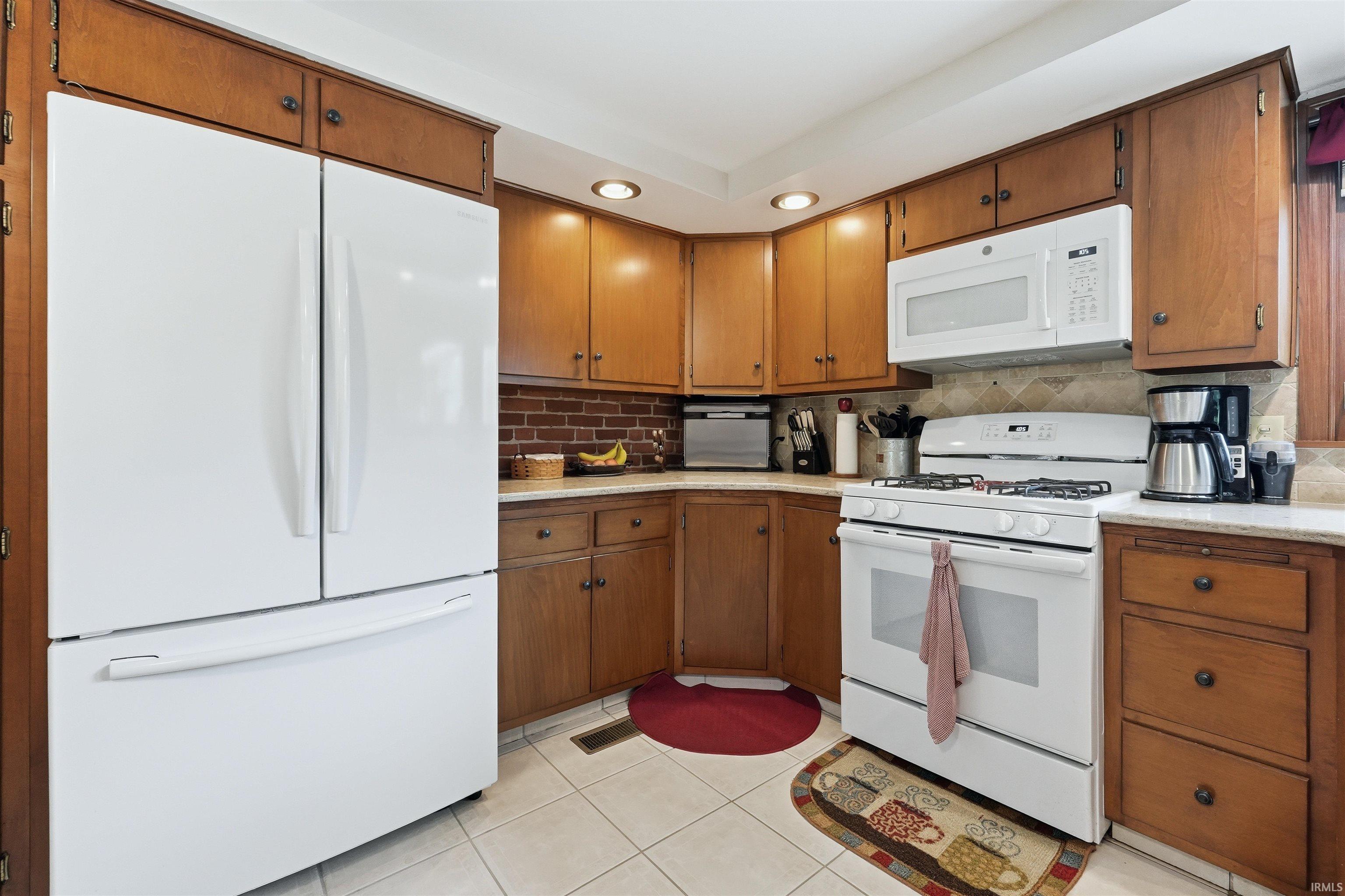 Kitchen featuring wood cabinetry, white appliances, recessed lighting, and tile flooring