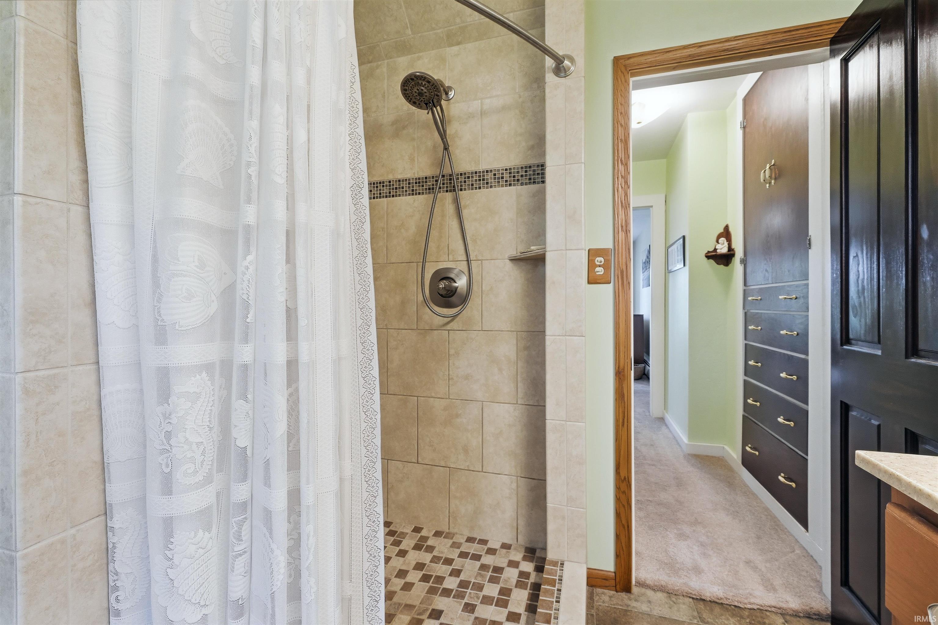 Tiled shower with mosaic floor and decorative band, featuring a handheld showerhead