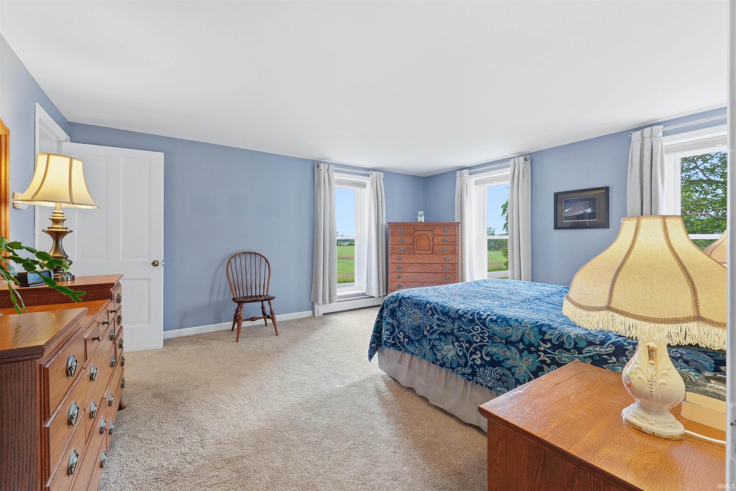 Spacious room featuring light blue walls, neutral carpet flooring, and multiple windows providing natural light