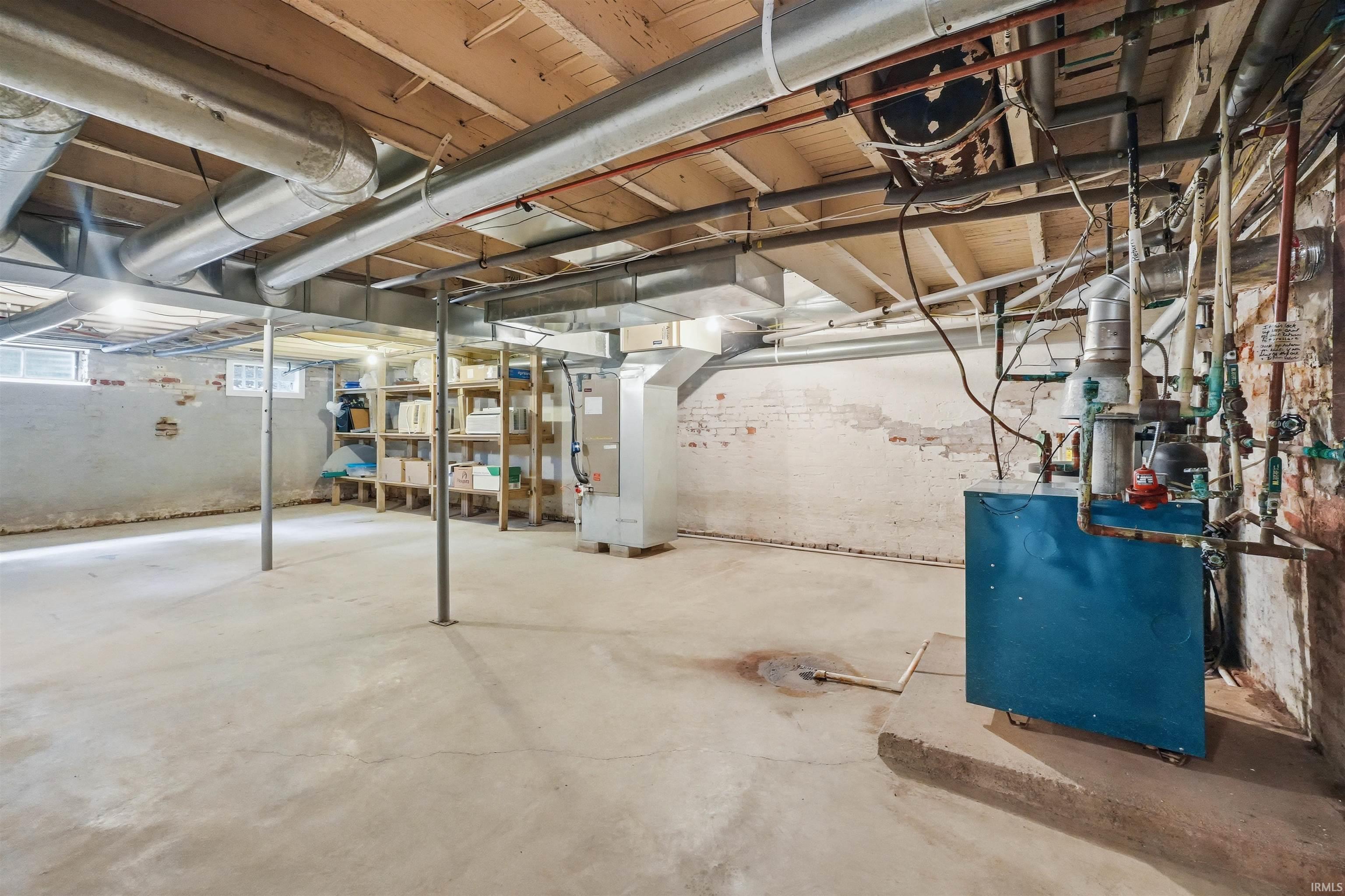 Unfinished basement featuring concrete flooring, exposed brick walls, visible mechanical systems, and structural support posts