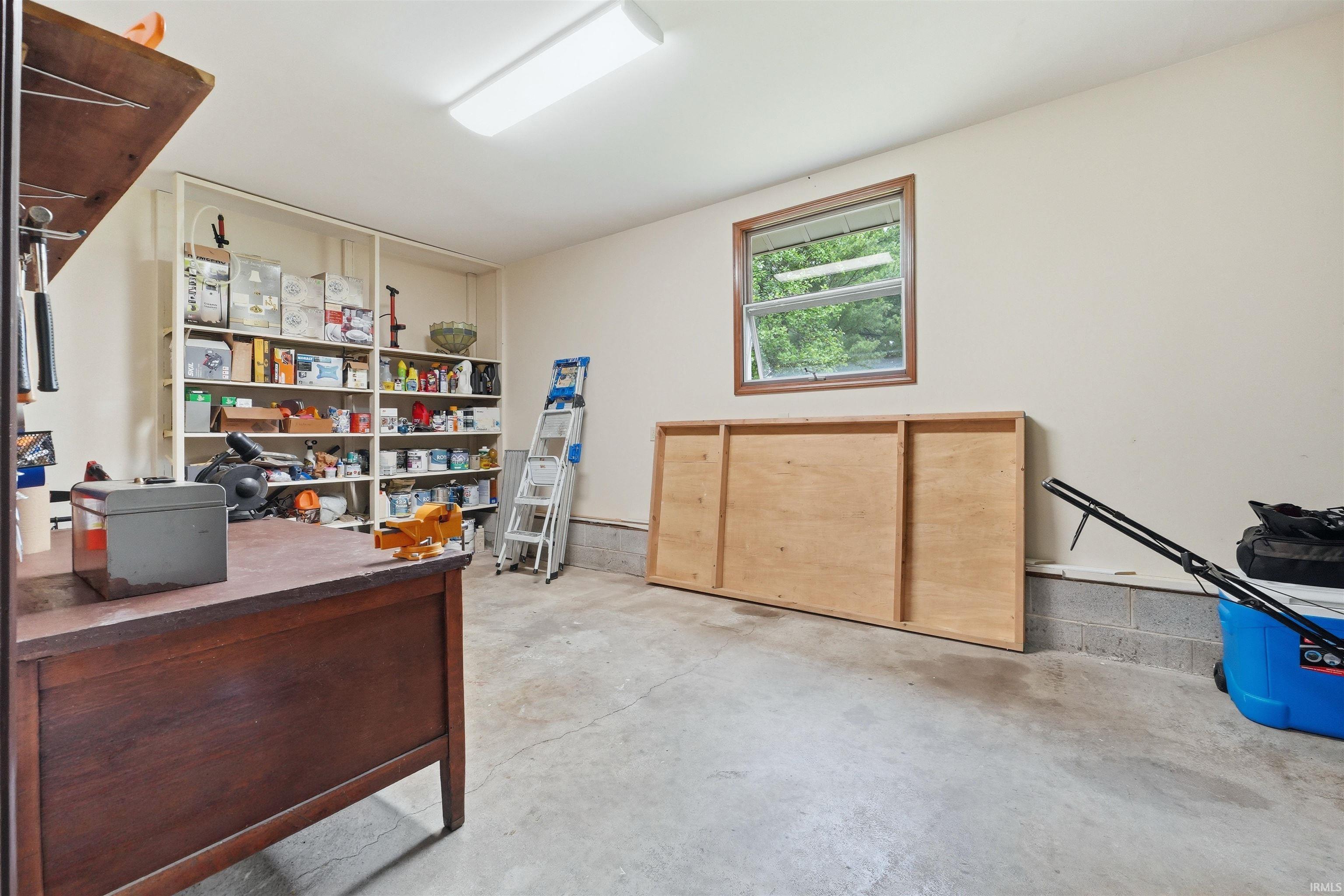 Spacious utility room featuring a large window, extensive built-in shelving, durable concrete flooring, and bright overhead lighting