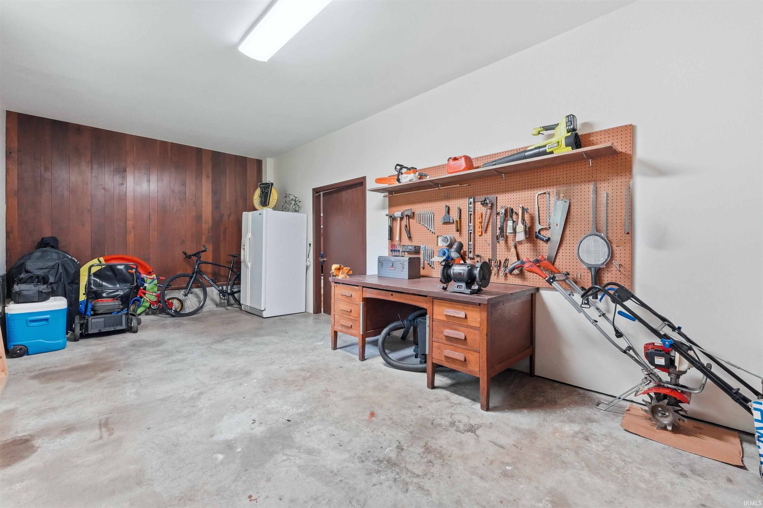 Spacious utility area featuring concrete flooring, a wood-paneled accent wall, a solid core door, and overhead fluorescent lighting