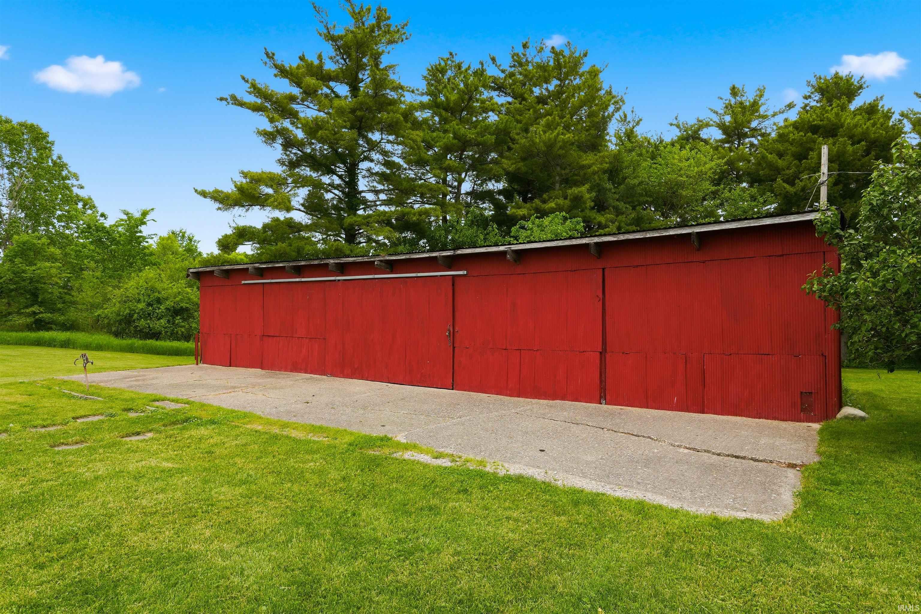 Red storage structure with multiple sliding barn doors, featuring a concrete pad and expansive green lawn