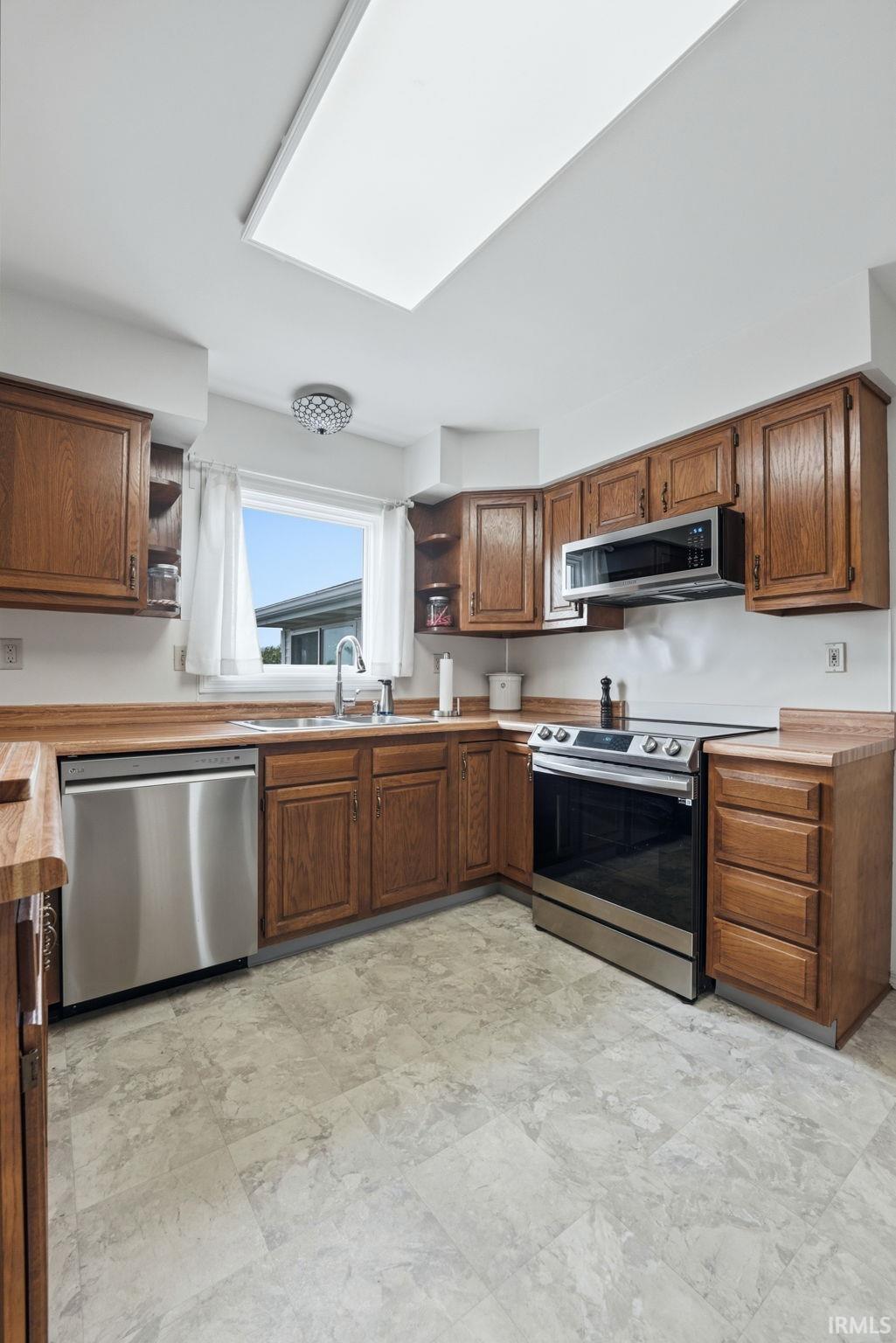 Kitchen featuring wood-finish cabinetry, stainless steel appliances, a window with natural light, and a large overhead light panel