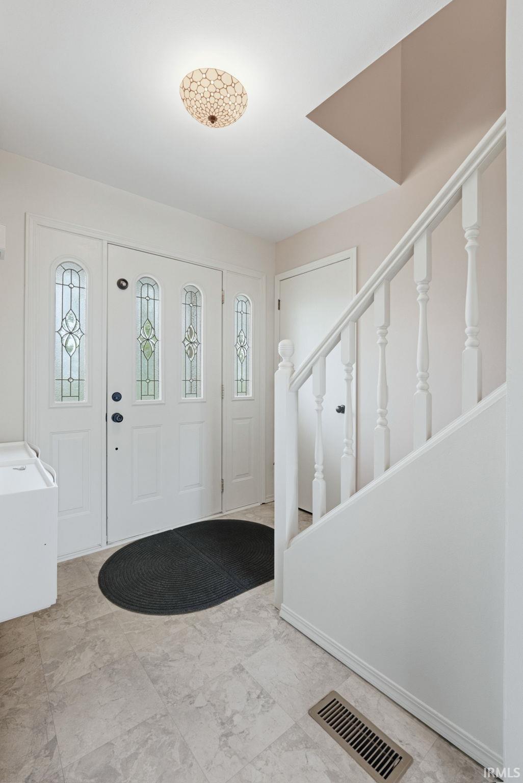 Entryway featuring a decorative main door with frosted glass panels and sidelights, durable tile flooring, white baluster staircase, and a contemporary flush-mount ceiling light fixture
