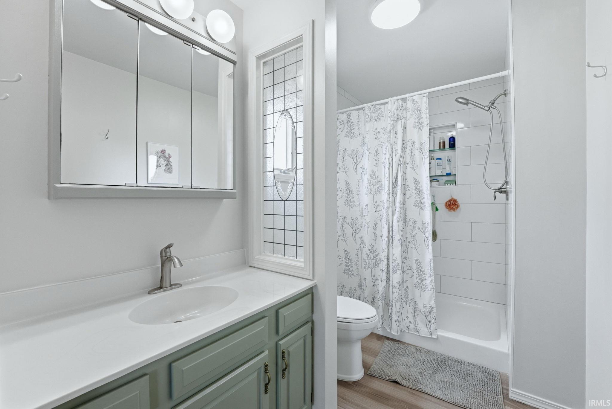 Bathroom featuring a vanity with an integrated sink, a three-door mirrored medicine cabinet, a decorative privacy window, and a shower-over-tub combination with white subway tile