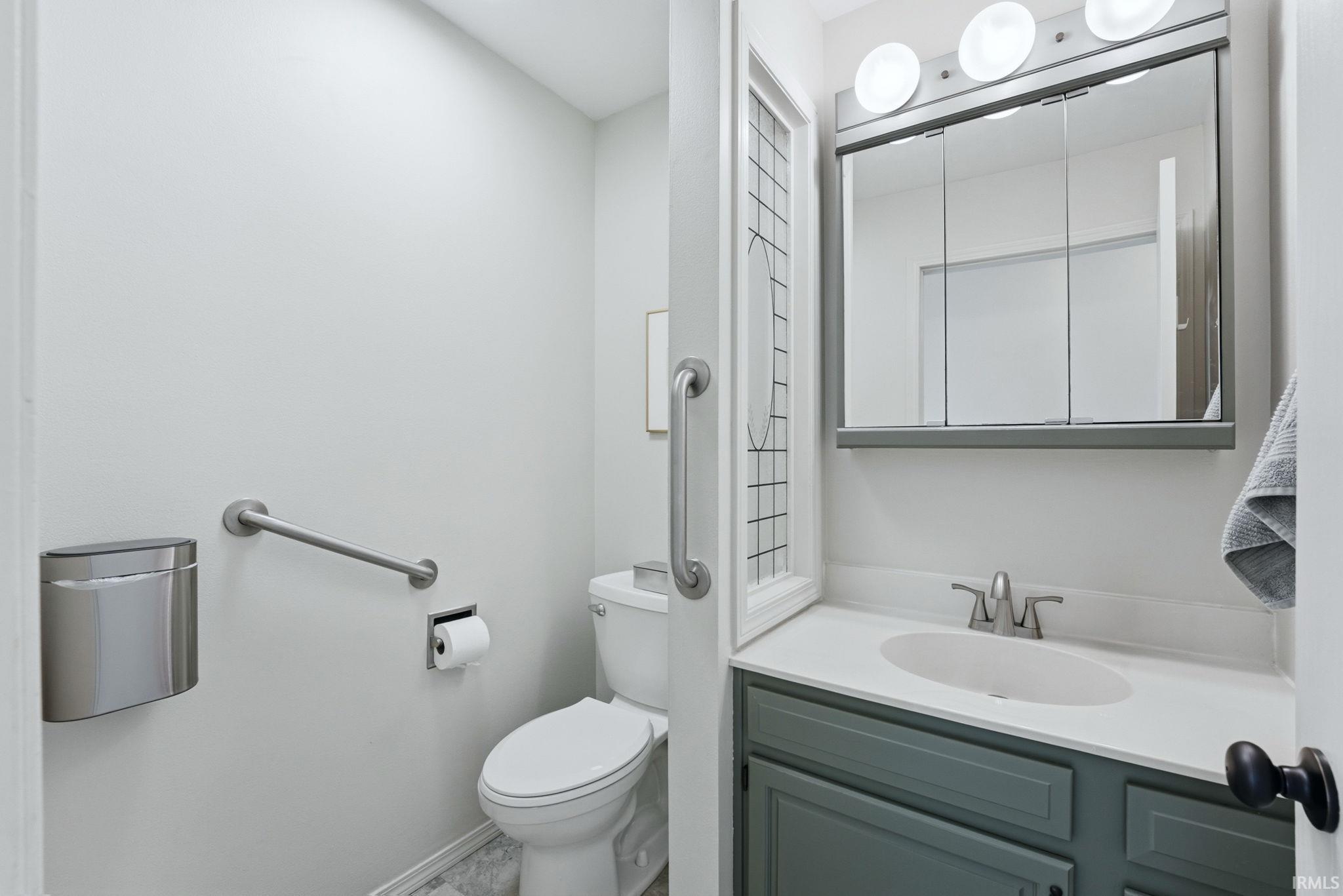 Bathroom featuring a white vanity countertop with an integrated sink, a gray vanity cabinet, and a multi-panel medicine cabinet with integrated lighting